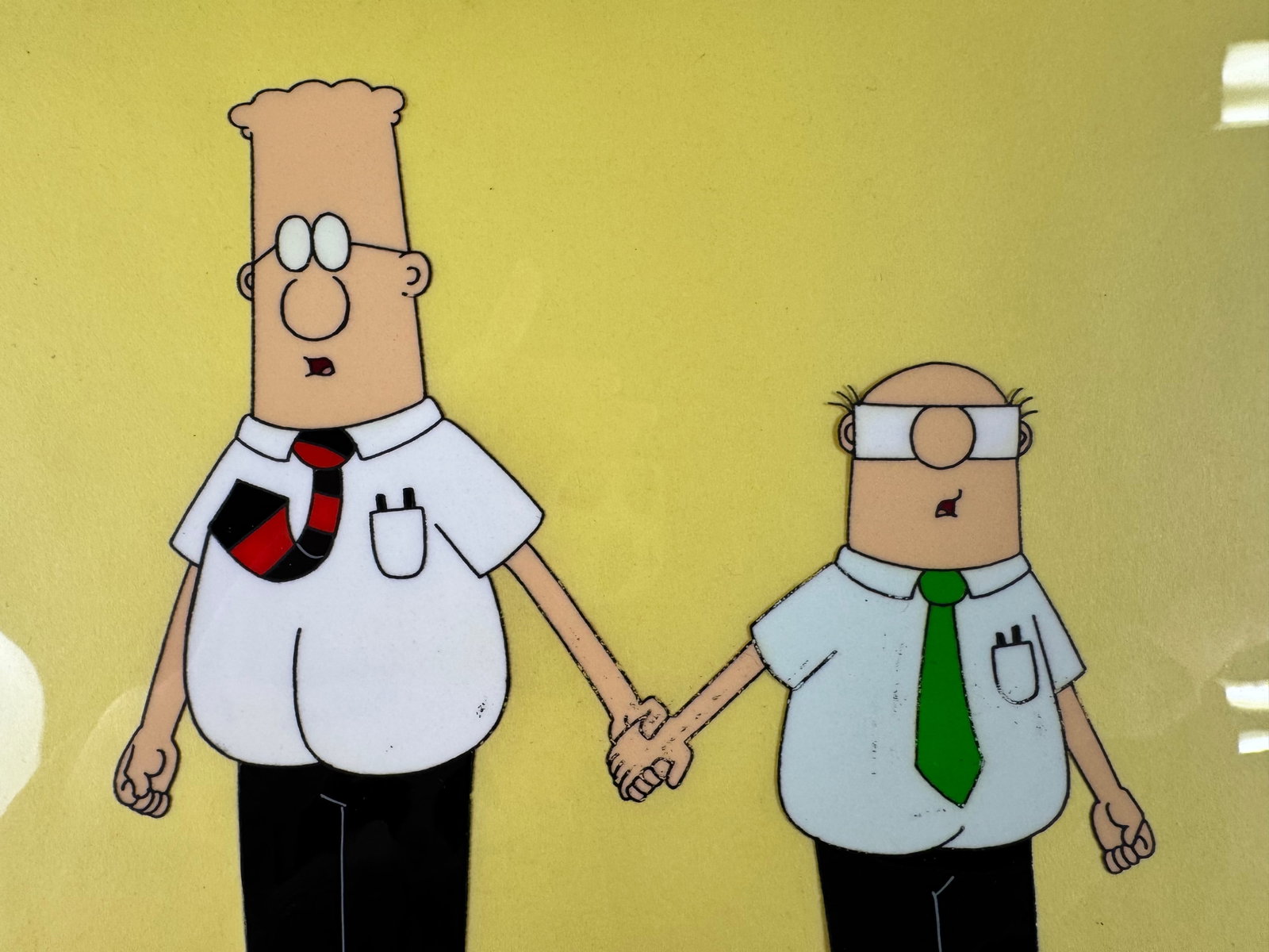 Dilbert Original Animation Production Cel Dilbert and Wally Signed Seth Kearsley COA: This original animation production cel depicts Dilbert and Wally holding hands against a yellow background. The cel is signed by Seth Kearsley and includes a certificate of authenticity.