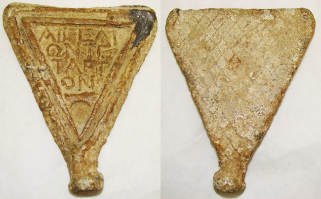 Roman Colonial, a lead weight as inverted triangle: Roman Colonial, c. 300-100BC., a lead weight in the shape of an inverted triangle with small flat ball shaped base. On front side are 4 lines of raised Greek text and an outstretched arm and hand at b