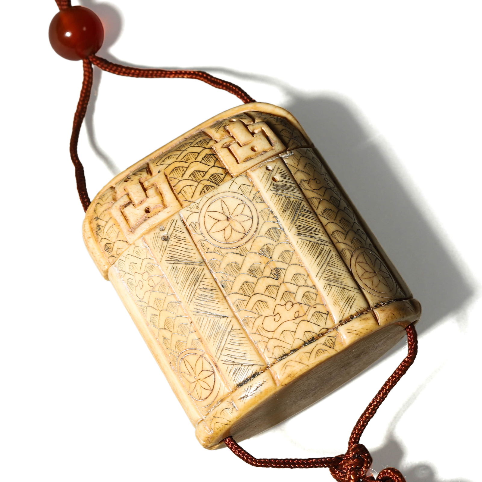 CARVED BONE INRO-FORM PENDANT BOX: Dimensions: Length: 1 7/8 in. (4.7 cm), Width: 1 11/16 in. (4.3 cm) Description: This intricately carved bone inro-style pendant box is adorned with traditional Japanese motifs including geometric pat