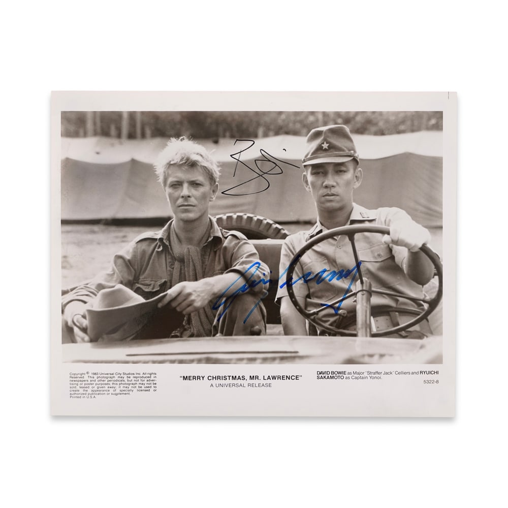DAVID BOWIE & RYUICHI SAKAMOTO SIGNED "MERRY CHRISTMAS, MR. LAWRENCE" PUBLICITY STILL (1983): 9 7/8 x 8 1/8 in (25.2 x 20.5 cm) Provenance and Authentication: This collectible has undergone a rigorous forensic evaluation. The signatures were carefully analyzed across multiple criteria, includi