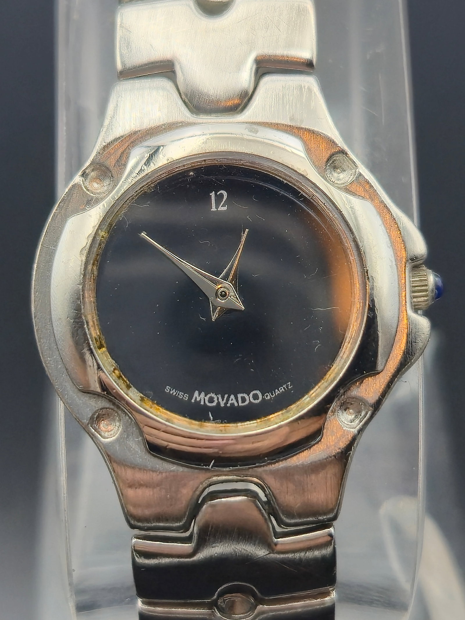 Movado Women's Quartz Watch – Model 47A4082N, Black Dial, Stainless Steel: This elegant Movado women’s quartz wristwatch features a sleek black dial with minimalist styling, highlighted by a single numeral at 12 o'clock and polished silver-tone dauphine hands. The case and