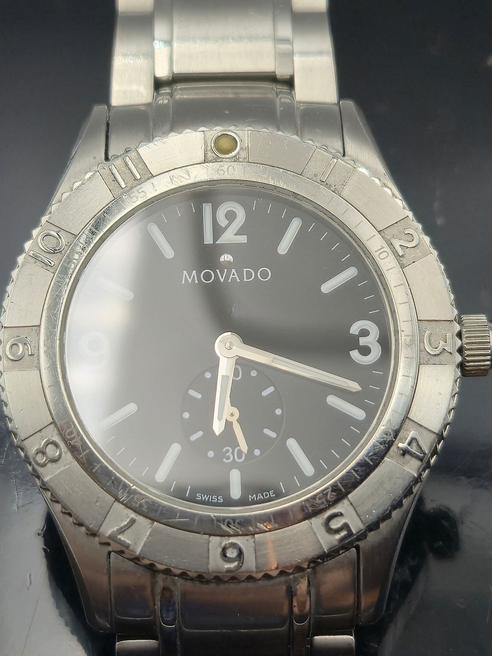 Movado 84 N2 1890 Stainless Steel Swiss Quartz Watch: Stylish and robust, this Movado Swiss-made stainless steel wristwatch features a clean black dial with bold white hour markers and luminous hands. The watch includes a sub-seconds dial at 6 o'clock, q