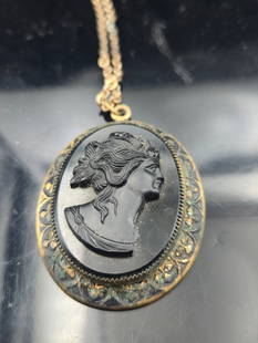 Vintage Black Cameo Pendant Necklace – Ornate Gold-Tone Frame, Floral Design – Circa: This striking vintage necklace features a beautifully carved black cameo depicting a classical female profile, set in an ornate oval gold-tone frame with an intricate floral motif. The pendant hangs f