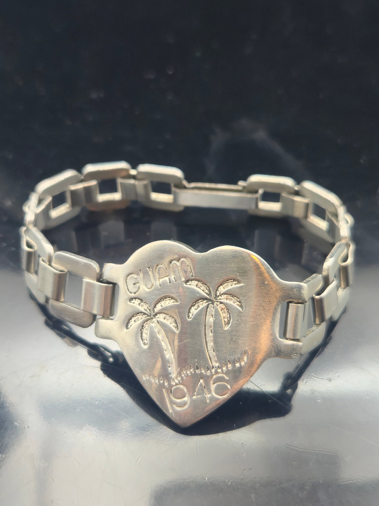 1946 Guam Sterling Sweetheart Bracelet – WWII Era Heart Charm with Expansion Link Band: Offered is an original post-WWII sweetheart souvenir bracelet, dated 1946, featuring a sterling silver heart-shaped centerpiece engraved with "GUAM", twin palm trees, and a dotted shoreline motif. The