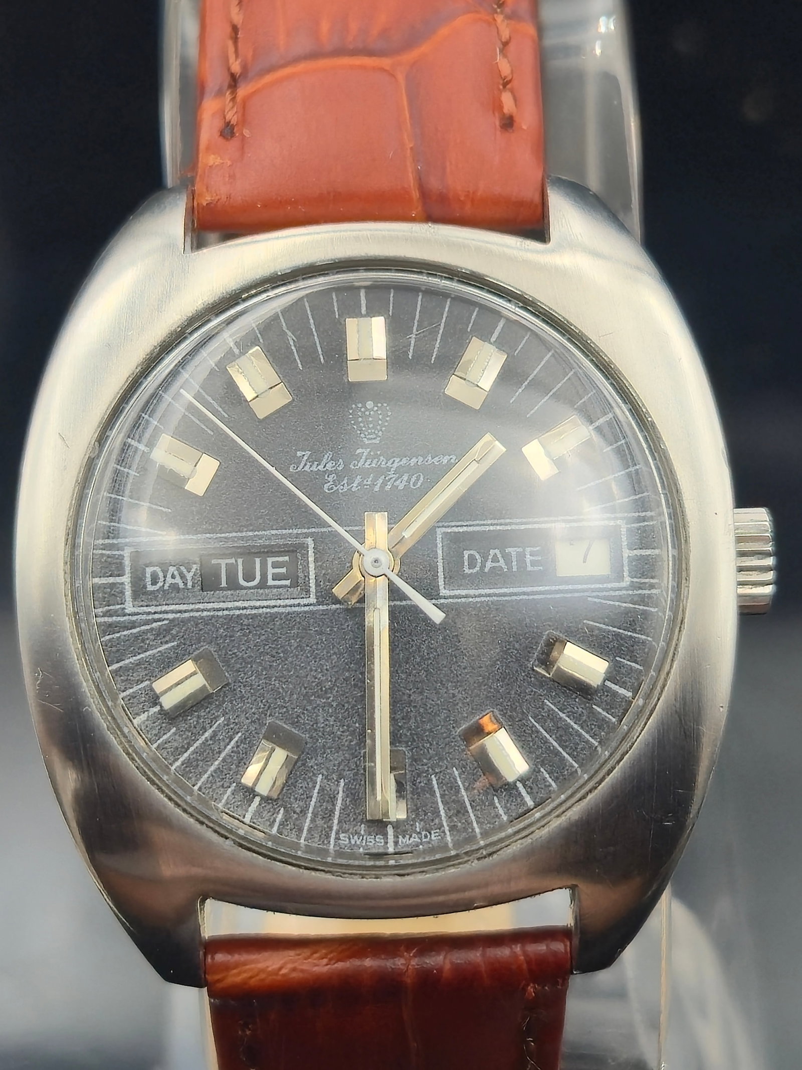 Vintage Jules Jürgensen Est. 1740 Swiss Day-Date Watch – 17J Manual Wind, Circa 1970s: This is a vintage Jules Jürgensen Est. 1740 Swiss-made wristwatch featuring a bold brushed black dial with dual apertures for both day and date displays. The watch is powered by a manual wind 17-jewe