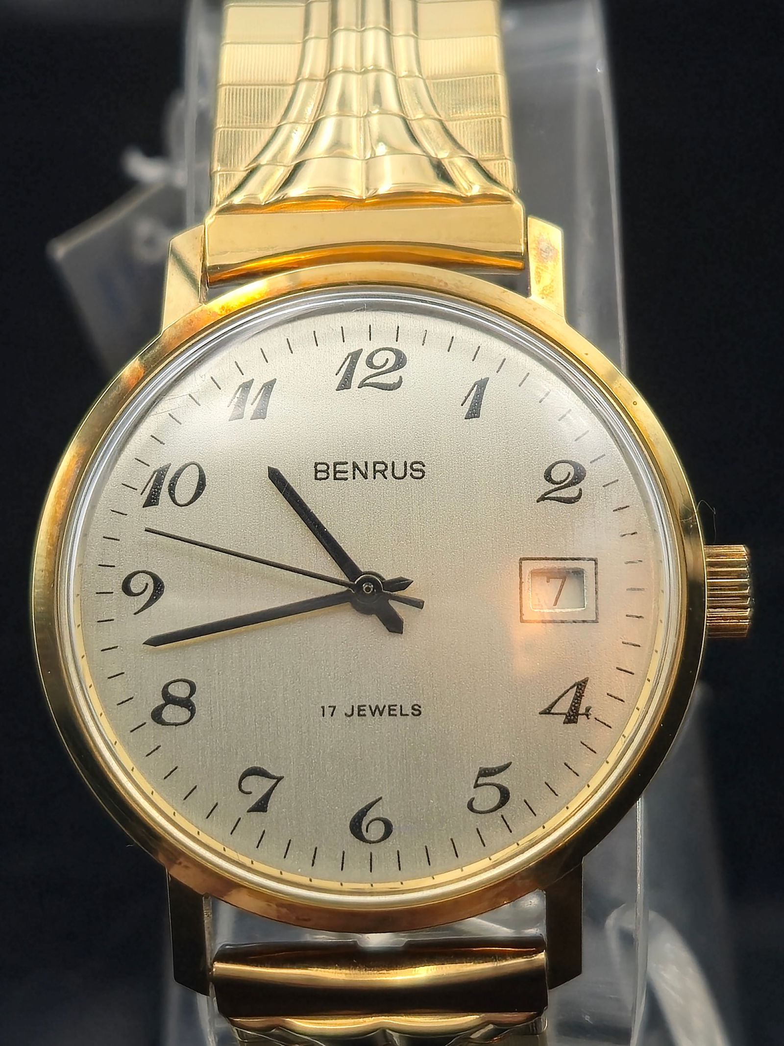NOS Benrus D-228F Calendar 17 Jewels Wristwatch – Full Set – c.1980s: Offered here is a New Old Stock (NOS) Benrus D-228F men’s wristwatch, featuring a clean silver sunburst dial with Arabic numerals, black hands, and a framed date window at 3 o’clock. Powered by a