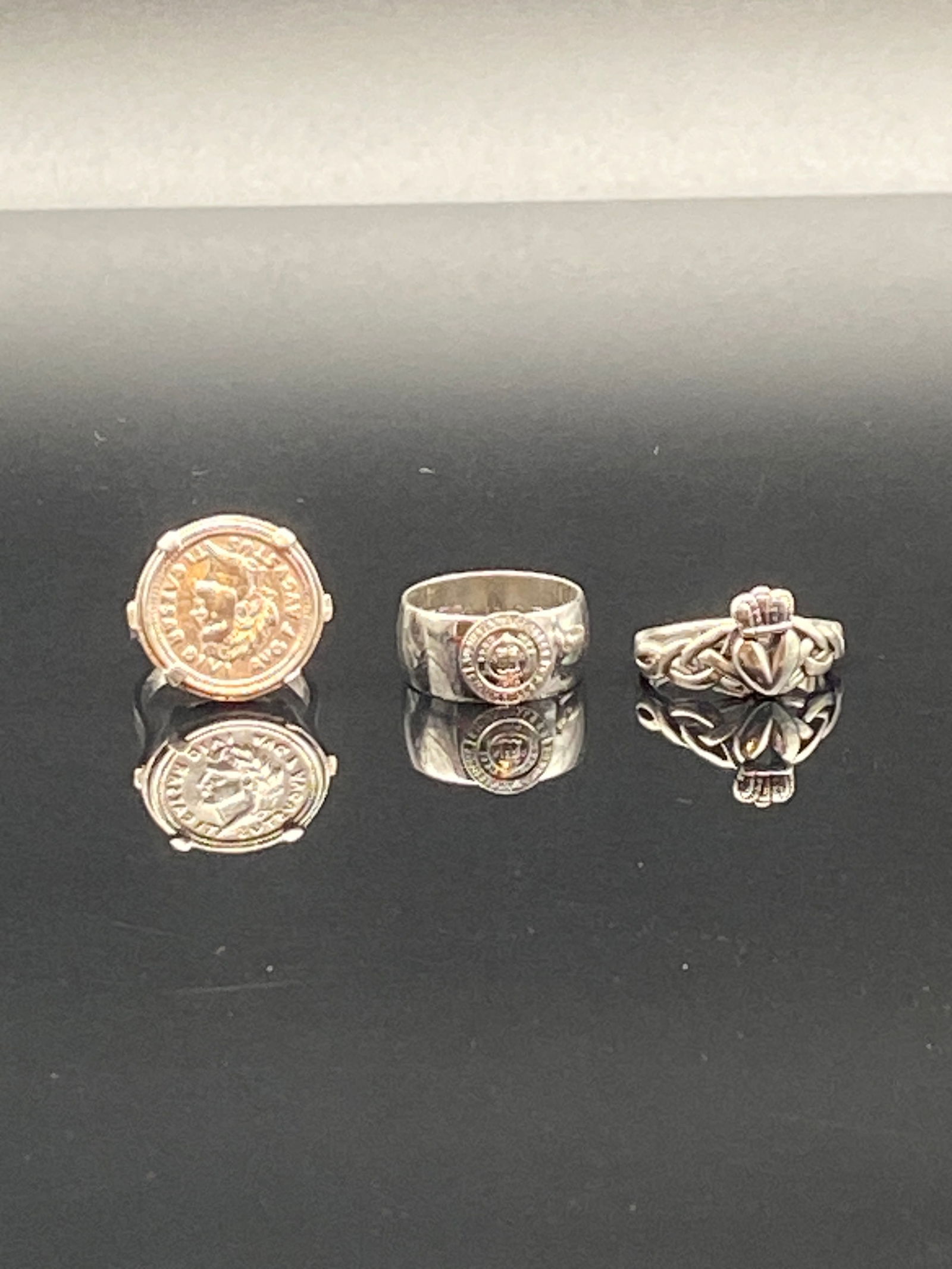Sterling Silver Rings – Coin, Compass, and Claddagh Designs: A distinctive set of sterling silver rings, each carrying strong symbolic motifs: 1.Ring One (Left)•Coin-style design featuring a raised profile portrait with surrounding inscriptions.•Bezel