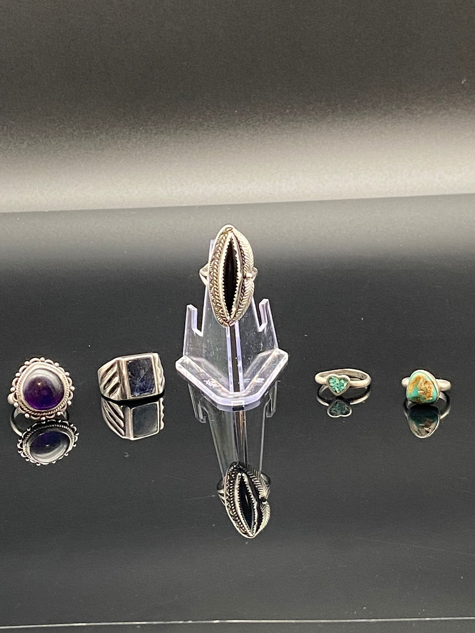 Collection of Five Sterling Silver Rings – Gemstone & Tribal Designs: A diverse lot of five sterling silver rings, featuring both natural stones and ethnic-inspired designs:1.Ring One (Far Left)•Round cabochon of deep purple (likely amethyst).•Surrounded by a