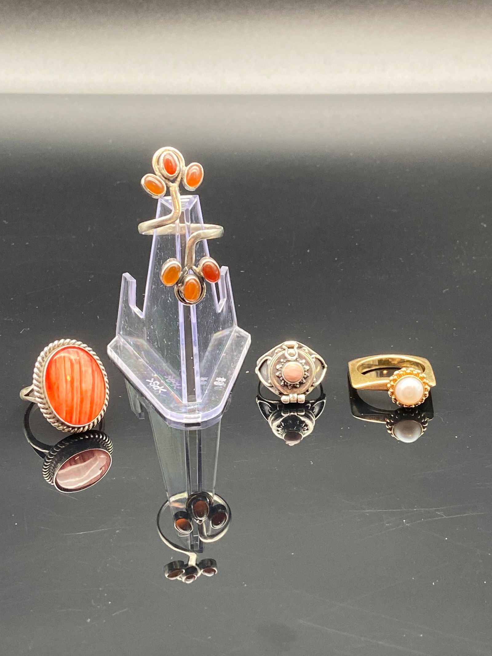 Sterling & Gold-Tone Rings – Coral, Carnelian & Pearl Accents: A striking mix of vintage rings in silver and gold-tone settings, highlighted by bold orange-red and soft pearl hues:1.Ring One (Far Left)•Large oval cabochon in bright orange-red (likely coral o