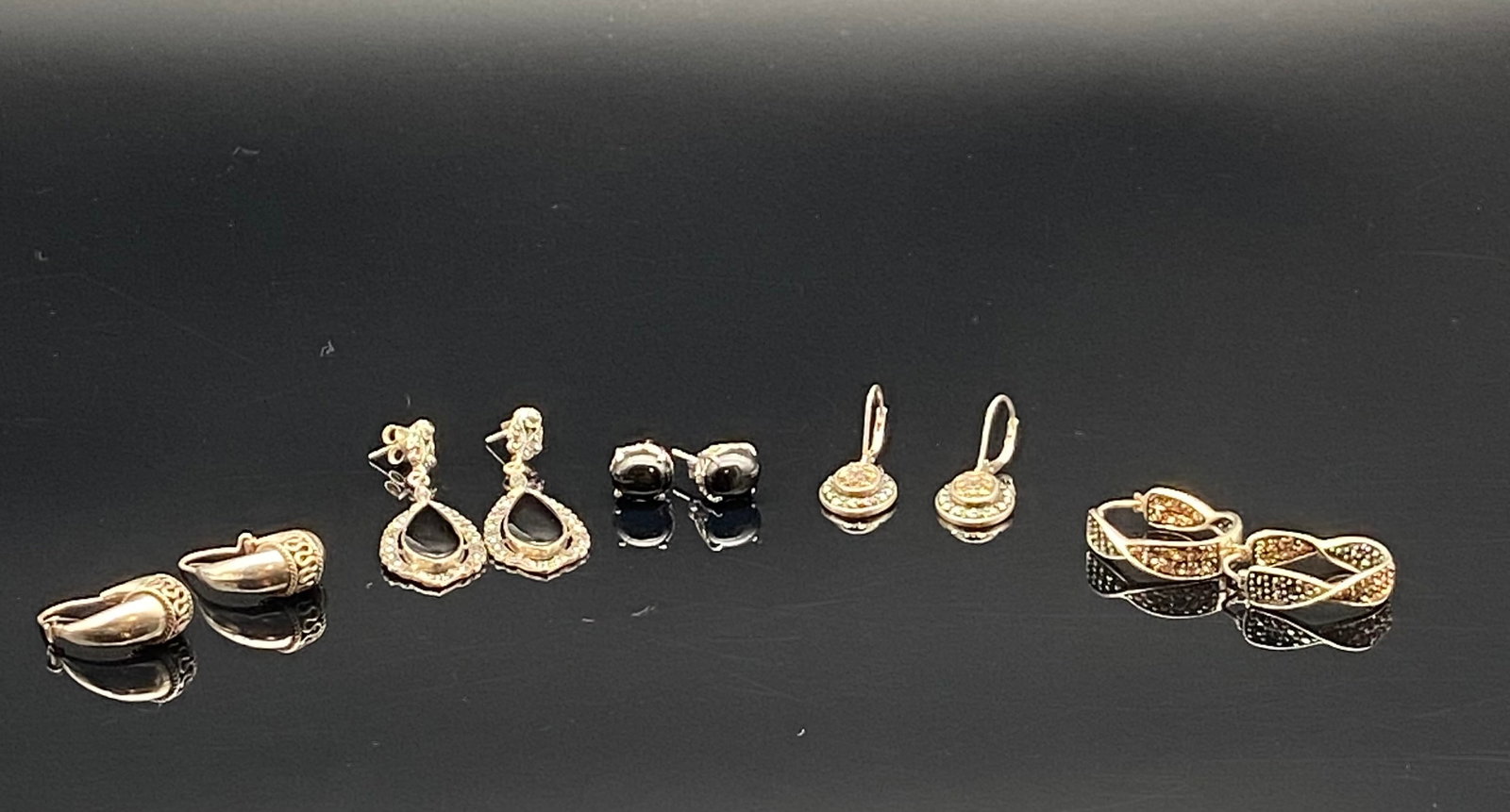 Five Pairs Sterling Silver Earrings with Onyx Accents: A diverse set of five pairs of sterling silver earrings, each with its own unique design and character:•Far Left: Teardrop-shaped silver earrings with ornate top detailing.•Left Center: Eleg