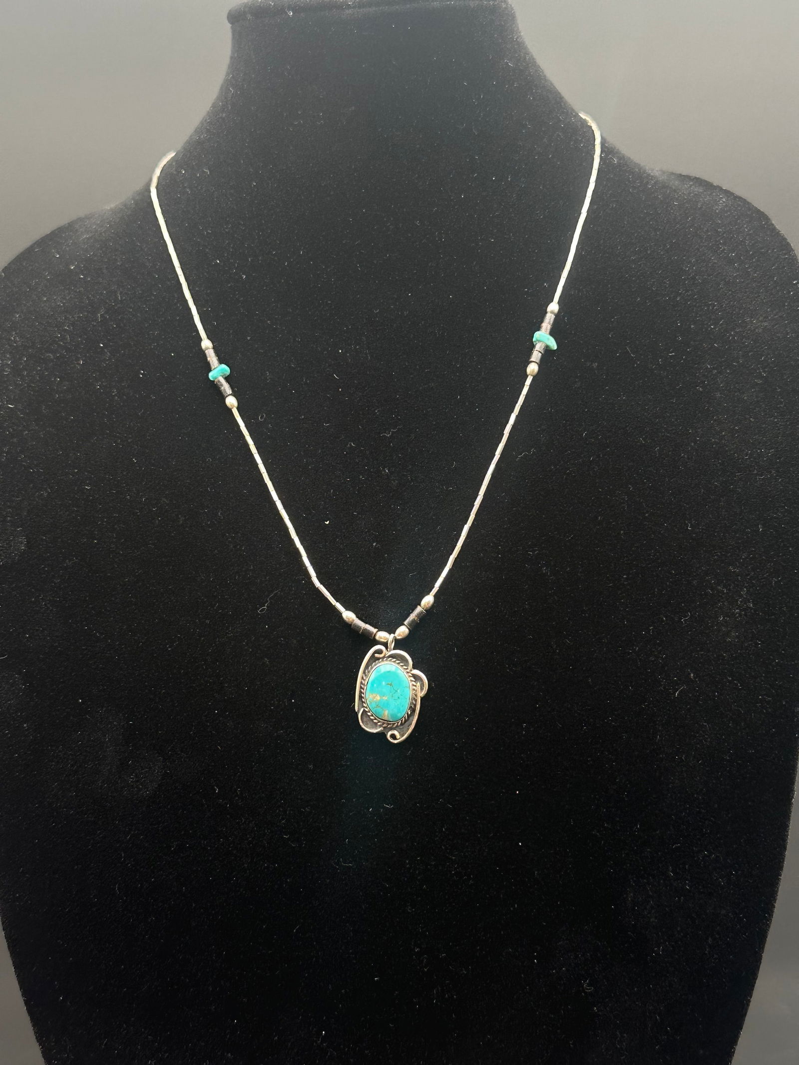 Sterling Silver Beaded Necklace w/ Turquoise Pendant: Sterling silver beaded necklace with turquoise heishi accents, featuring an ornate pendant set with an oval turquoise cabochon. The stone displays bright blue hues with golden matrix. Classic Southwes