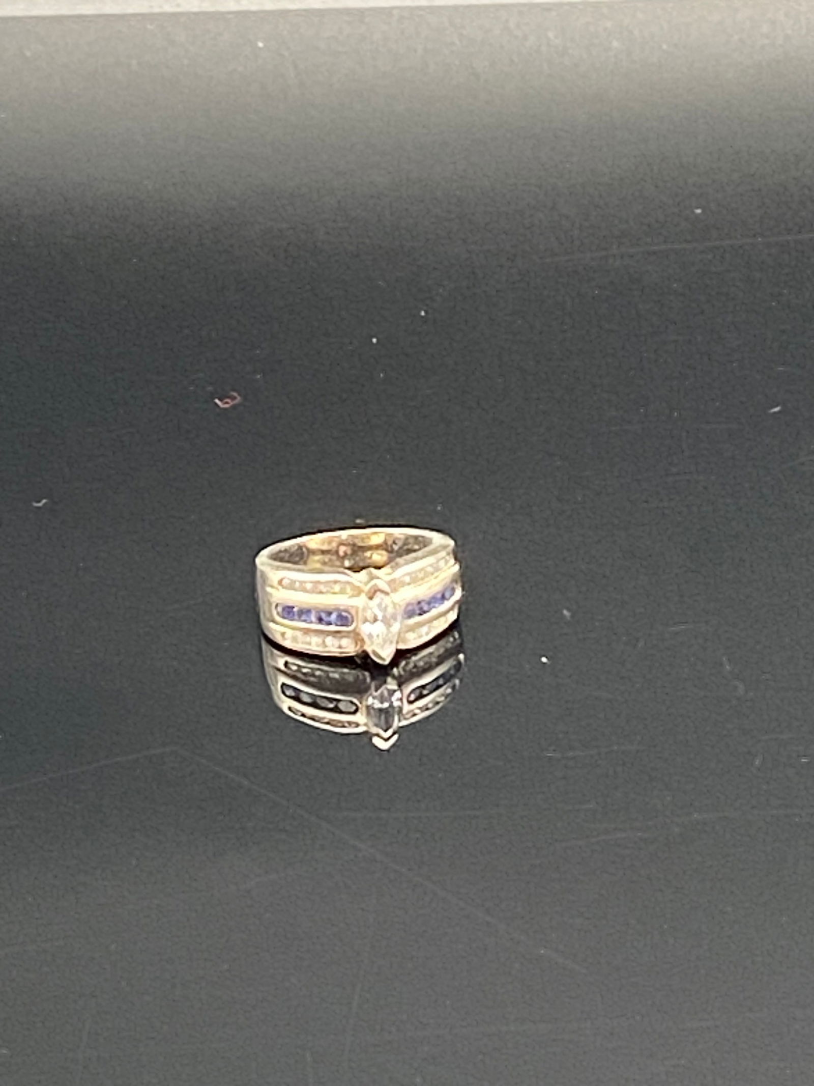 Vintage Silver CZ & Sapphire Accent: A bold vintage sterling silver ring featuring a marquise-cut clear CZ center stone, accented by channel-set blue sapphire-like stones and small clear accent stones on the shoulders. This wide band des