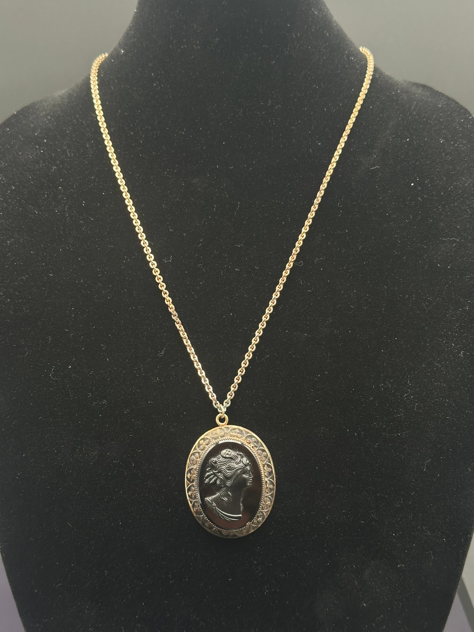 Vintage Gold-Tone Oval Cameo Pendant Necklace with Black Stone: Elegant vintage oval pendant necklace featuring a raised black stone cameo of a classical woman’s profile. The cameo is framed in a detailed gold-tone filigree border with floral and scroll motifs. 