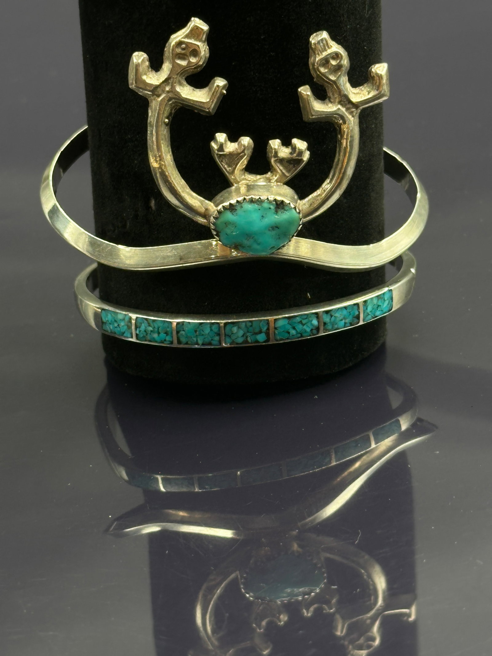 Pair of Sterling Silver Cuff Bracelets with Turquoise Inlay & Symbolic Motifs: A set of two handcrafted sterling silver cuffs:•First cuff: Features a raised symbolic design with two stylized figures above a bezel-set turquoise cabochon. The design reflects tribal-inspired a