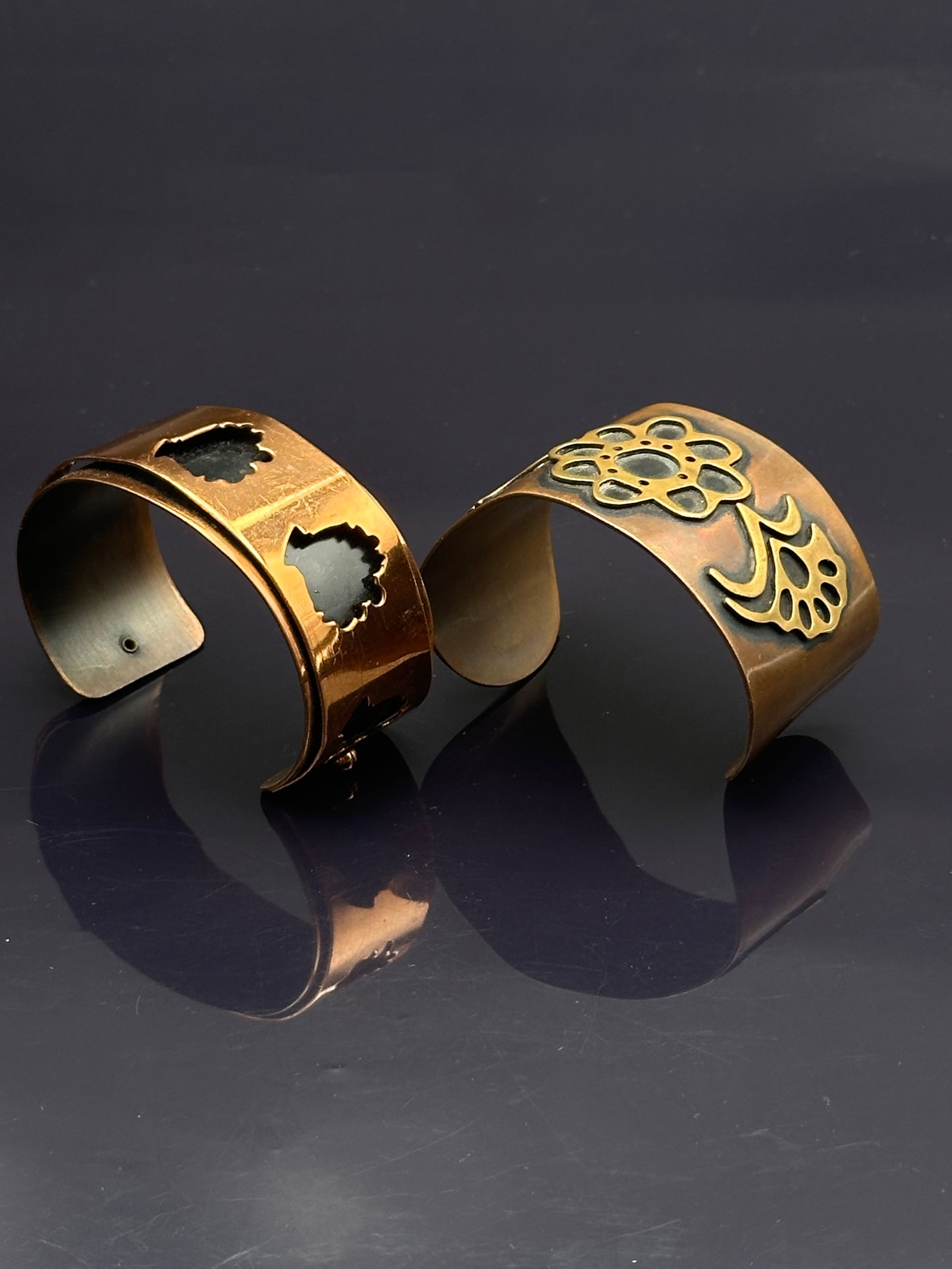 Pair of Vintage Copper Cuff Bracelets – Floral Overlay & Abstract Cut-Out Designs: Lot of two vintage genuine copper cuff bracelets featuring unique artisan designs:•Floral overlay cuff: Wide band with a bold flower and leaf cut-out overlay design in darkened relief.•Geome