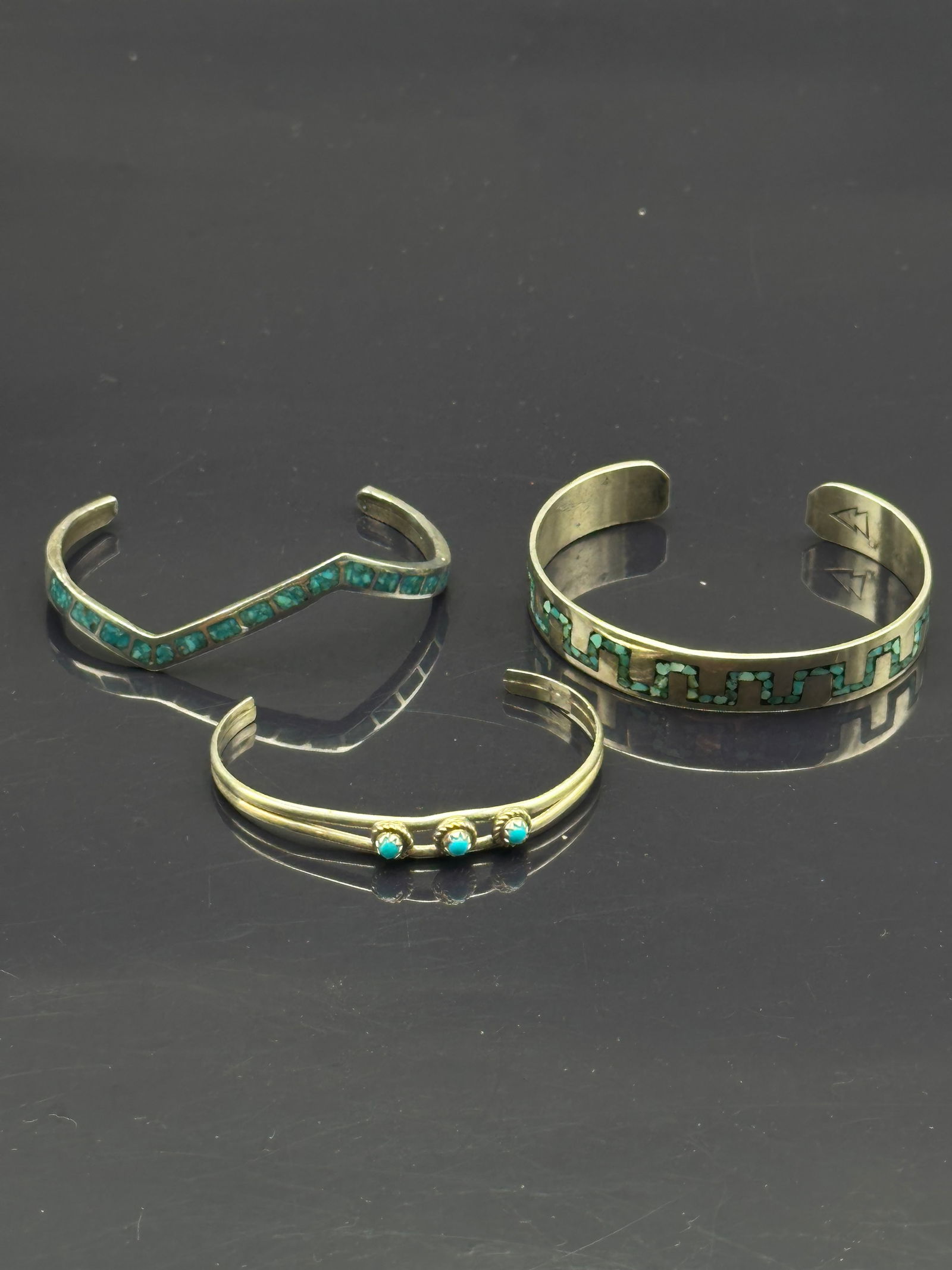 Lot of 3 Vintage Navajo/Zuni Sterling Silver Turquoise Cuff Bracelets – 28.3g: Collection of three vintage Native American sterling silver cuff bracelets: one featuring turquoise chip inlay in a geometric arrow/step motif (hallmarked with arrow symbol), one with square turquoise