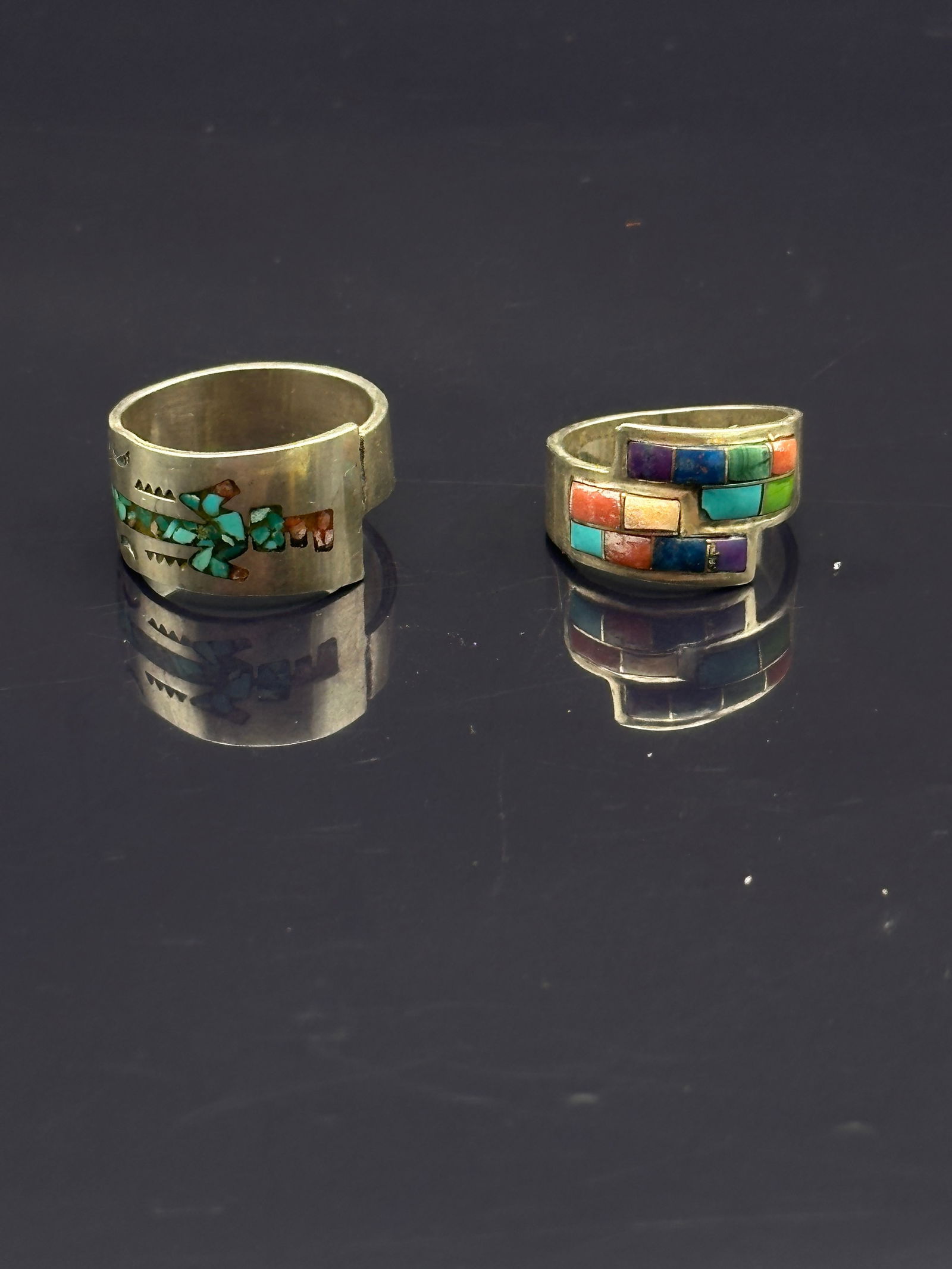 Pair of Vintage Native American Sterling Silver Inlay Rings: A striking pair of handcrafted Native American sterling silver rings featuring intricate stone inlay work. One band displays a traditional floral design inlaid with turquoise and coral, while the othe