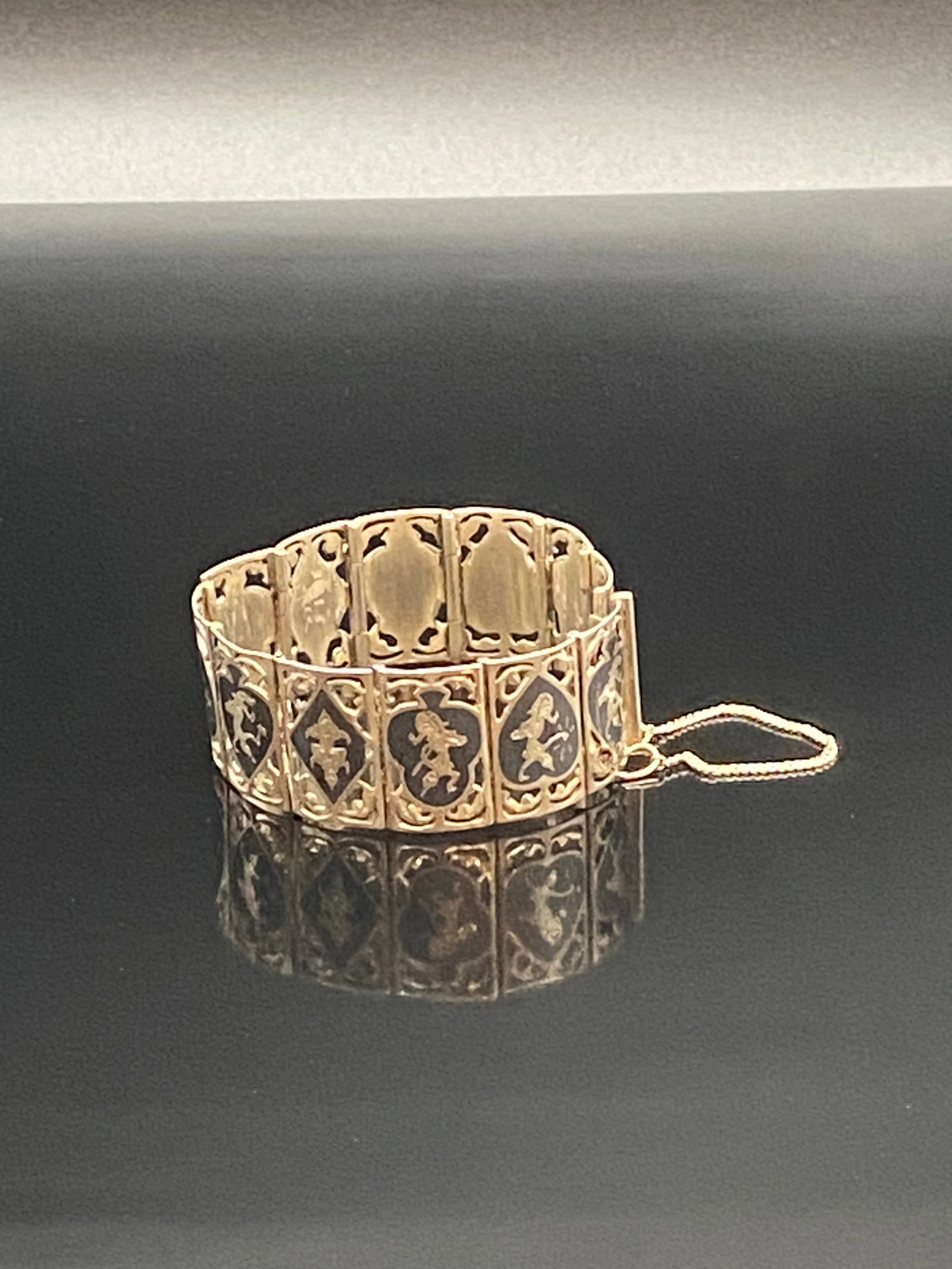 Vintage Gold-Plated Panel Bracelet with Safety Chain: An elegant vintage panel bracelet featuring ornate openwork designs with dark enamel-style accents and figural motifs. The bracelet consists of rectangular linked panels with intricate detailing, secu