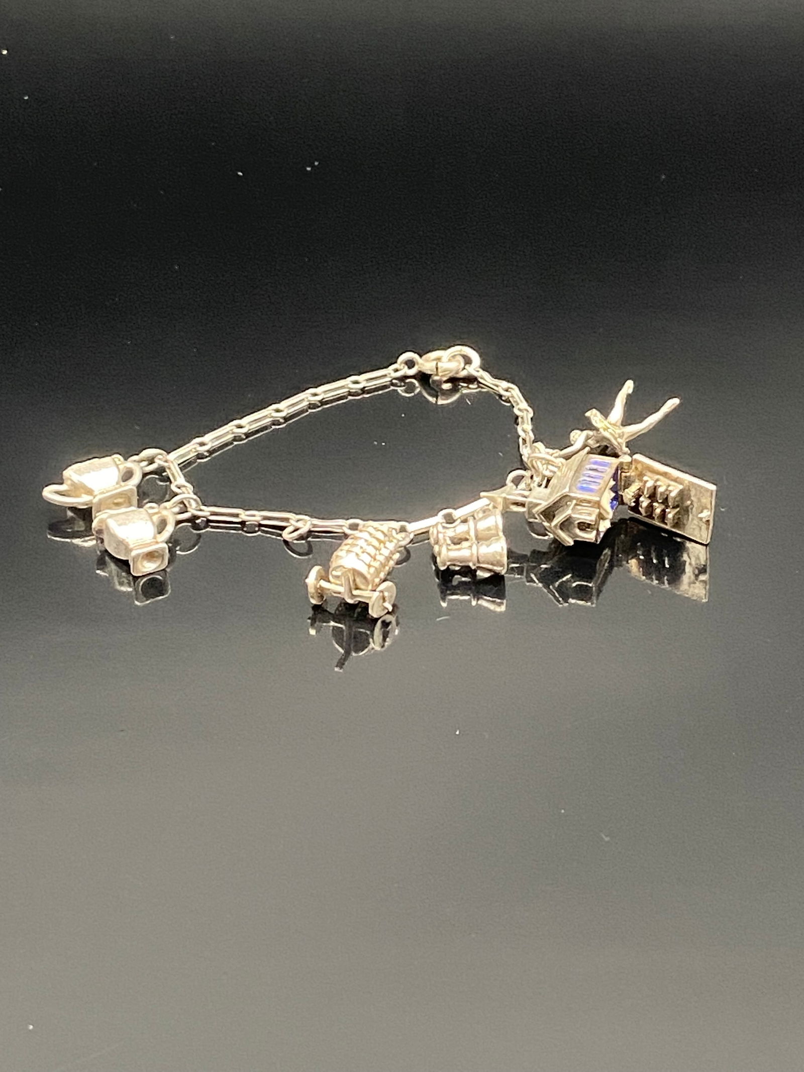 Vintage Sterling Silver Charm Bracelet: Charming vintage sterling silver bracelet featuring multiple detailed charms, including a typewriter, trunk, and other miniature figures. Each charm is securely attached to a link chain with a spring