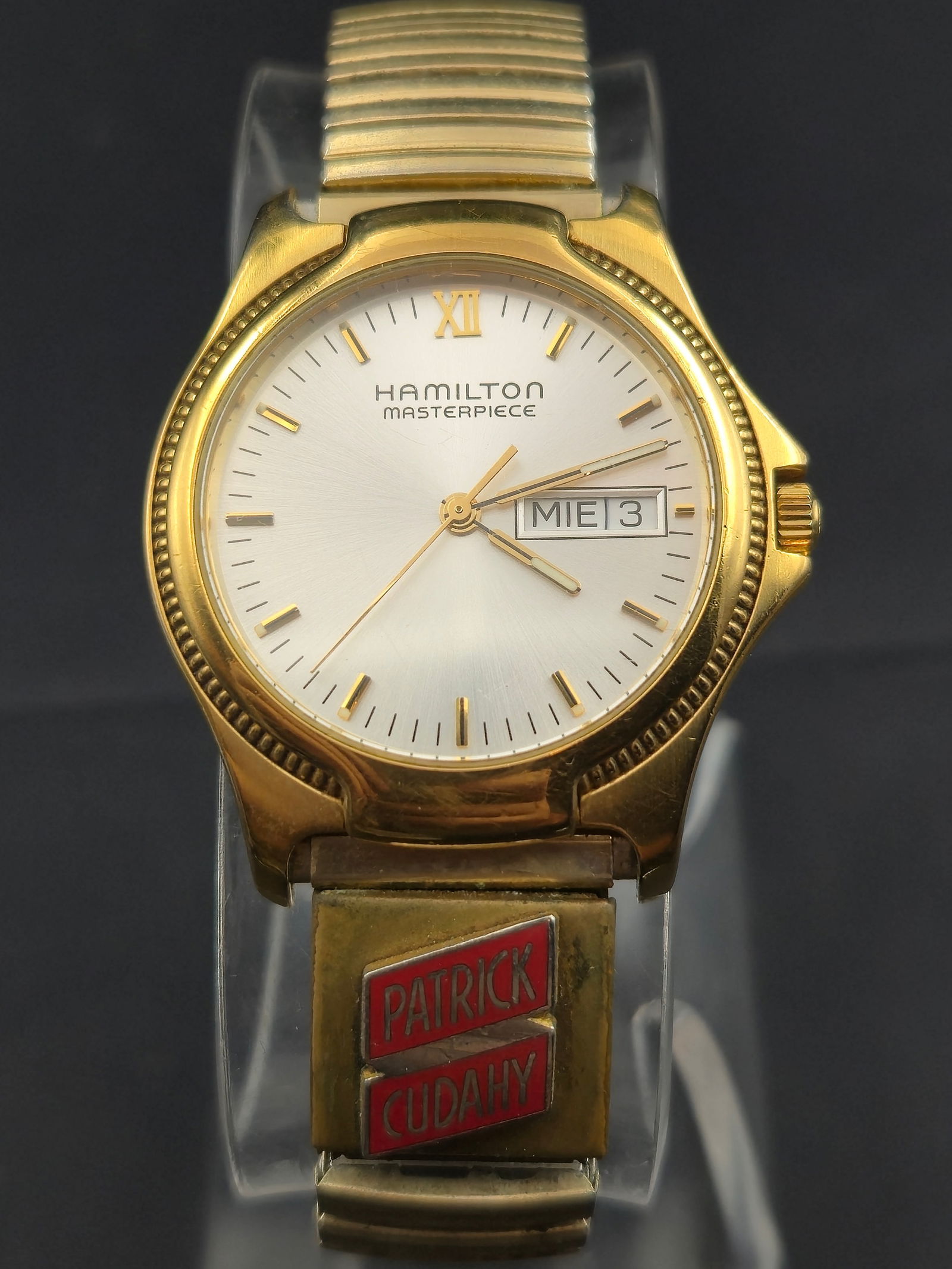 2002 Hamilton Masterpiece Quartz 34mm Gold-Tone Watch w/ Patrick Cudahy Band Running: Offered here is a 2002 Hamilton Masterpiece quartz wristwatch, reference 8458, paired with its original Speidel expansion bracelet featuring the red enamel Patrick Cudahy company logo clasp. This uniq