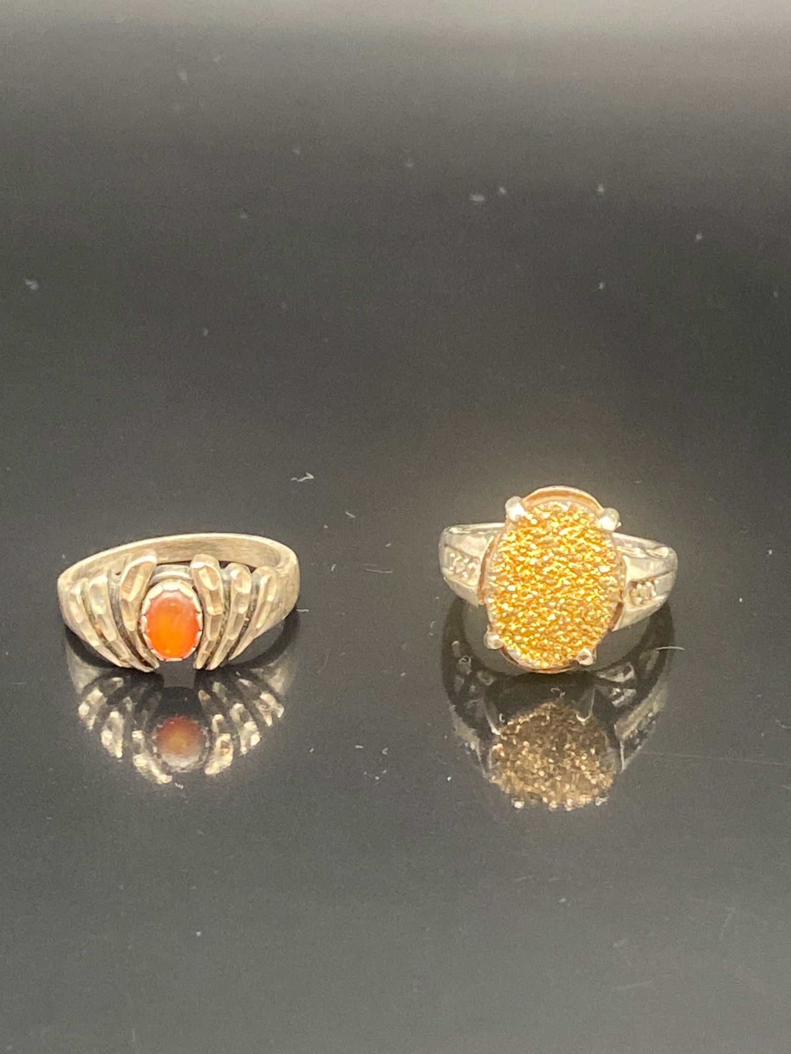 Pair of Sterling Silver Rings with Orange Gemstones: A vibrant duo of sterling silver rings, each featuring warm orange stones:•Left Ring: A unique silver band with claw-like side details, set with a glowing oval orange cabochon (resembling fire op