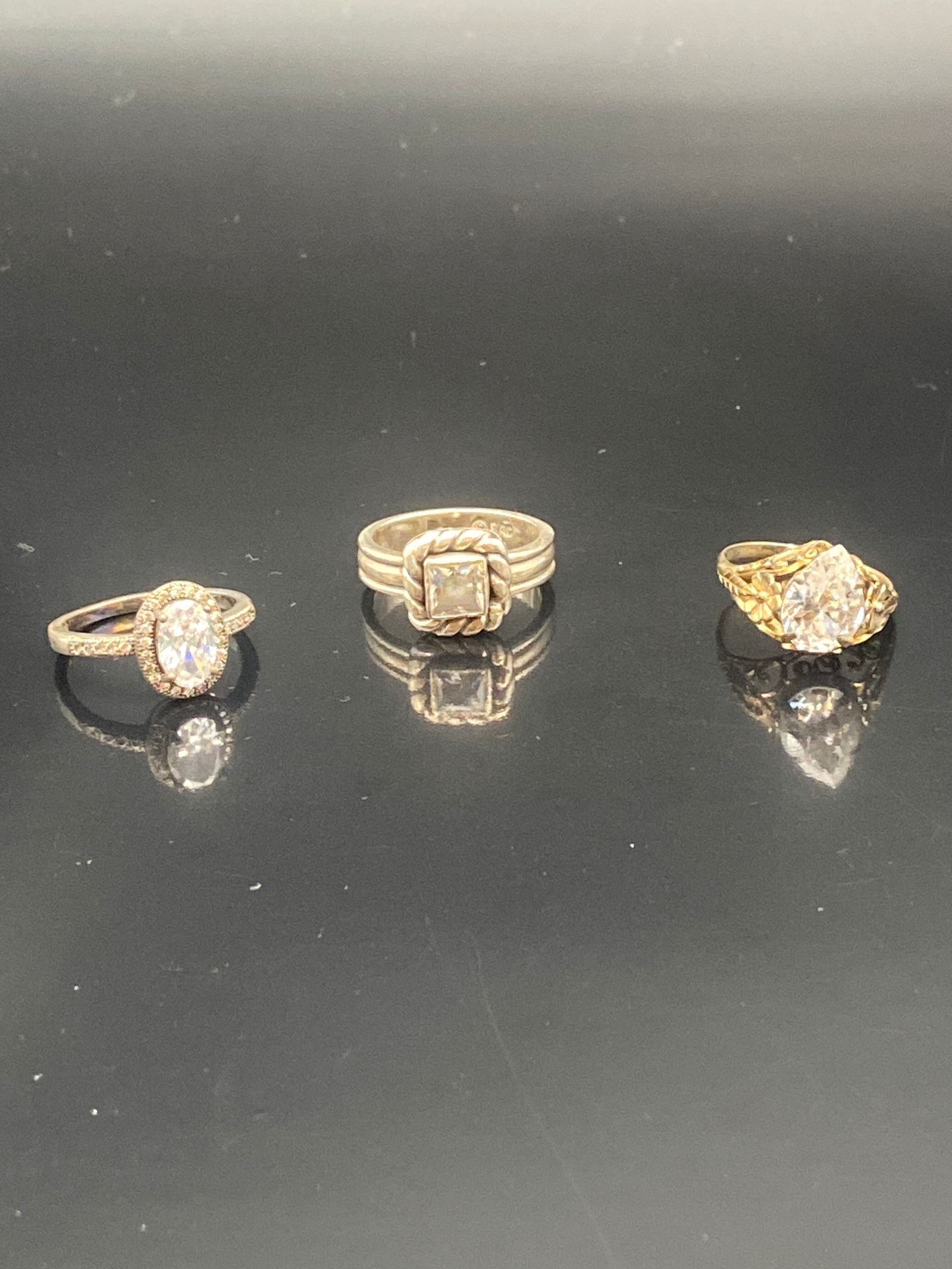 Set of Three Sterling Silver Rings with Clear Faceted Stones: A sparkling trio of sterling silver rings, each set with a clear faceted stone that mimics the brilliance of diamonds:•Left Ring: Round brilliant-cut stone framed in a halo of smaller clear stone