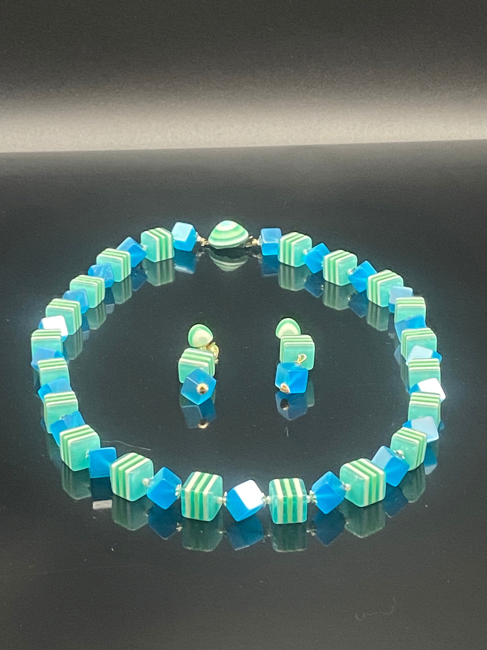Vintage Avon Striped Cube Bead Necklace & Matching Earrings Set – Blue & Green: This vibrant vintage Avon set includes a necklace and matching clip-on earrings crafted with bold geometric beads. The necklace alternates between striped green-and-white cube beads and translucent bl