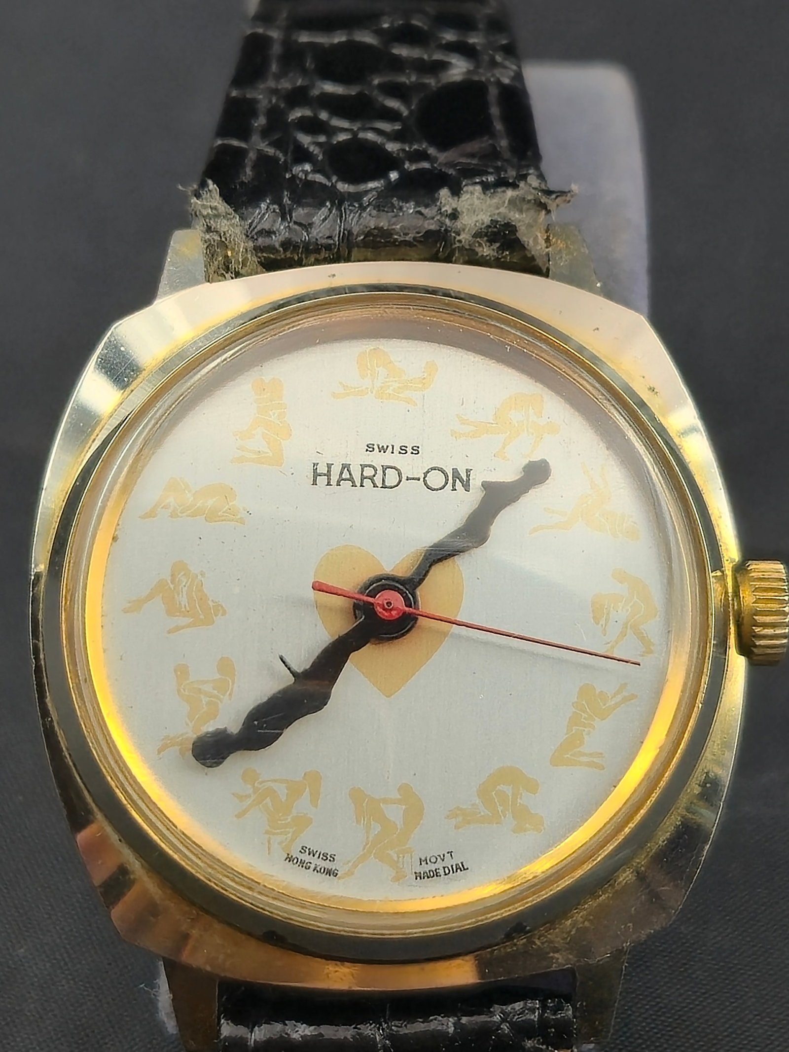 Swiss “Hard-On” Erotic Novelty Wristwatch 36mm Gold Tone Untested: A vintage Swiss “Hard-On” erotic novelty wristwatch, featuring a 36mm gold-tone case with stainless steel back and a black leather strap. The silver-tone dial is decorated with erotic figure i