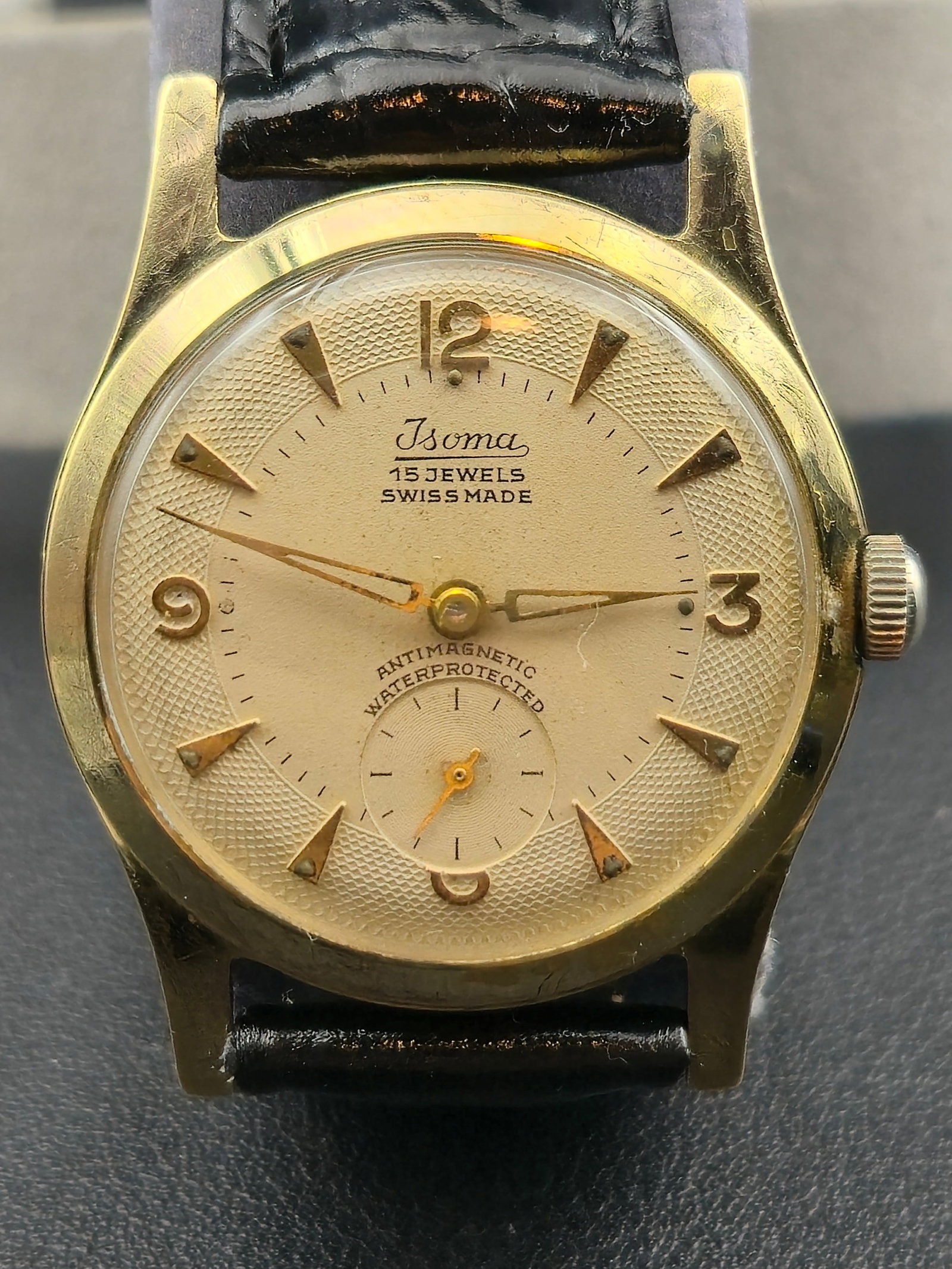 1950s Isoma “Textured Dial Dress Watch” Swiss 15J Manual Wind 32mm: Vintage Isoma Textured Dial Dress Watch featuring a Swiss-made 15-jewel manual-wind movement housed in a gold-tone case with a stainless-steel back. The champagne dial displays a guilloché-textured o