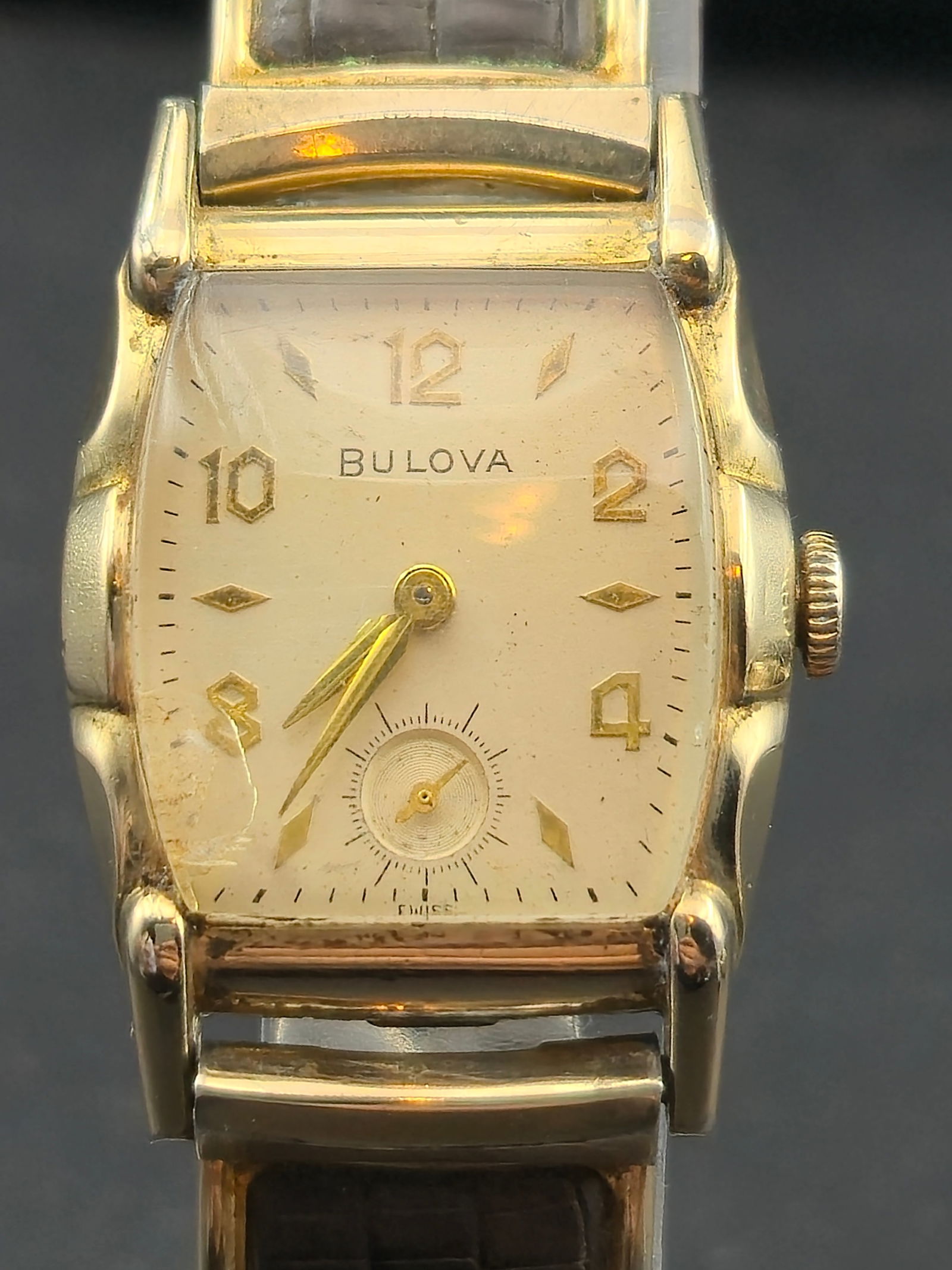 1955 Bulova 10K Rolled Gold Plate 25.5mm Tonneau Wristwatch w/ 10BT 15J Movement – Runs: Vintage Bulova wristwatch dated L5 (1955), showcasing mid-century American design in a curved tonneau-shaped case with elegant stepped lugs. The case is marked 10K rolled gold plate bezel with stainle