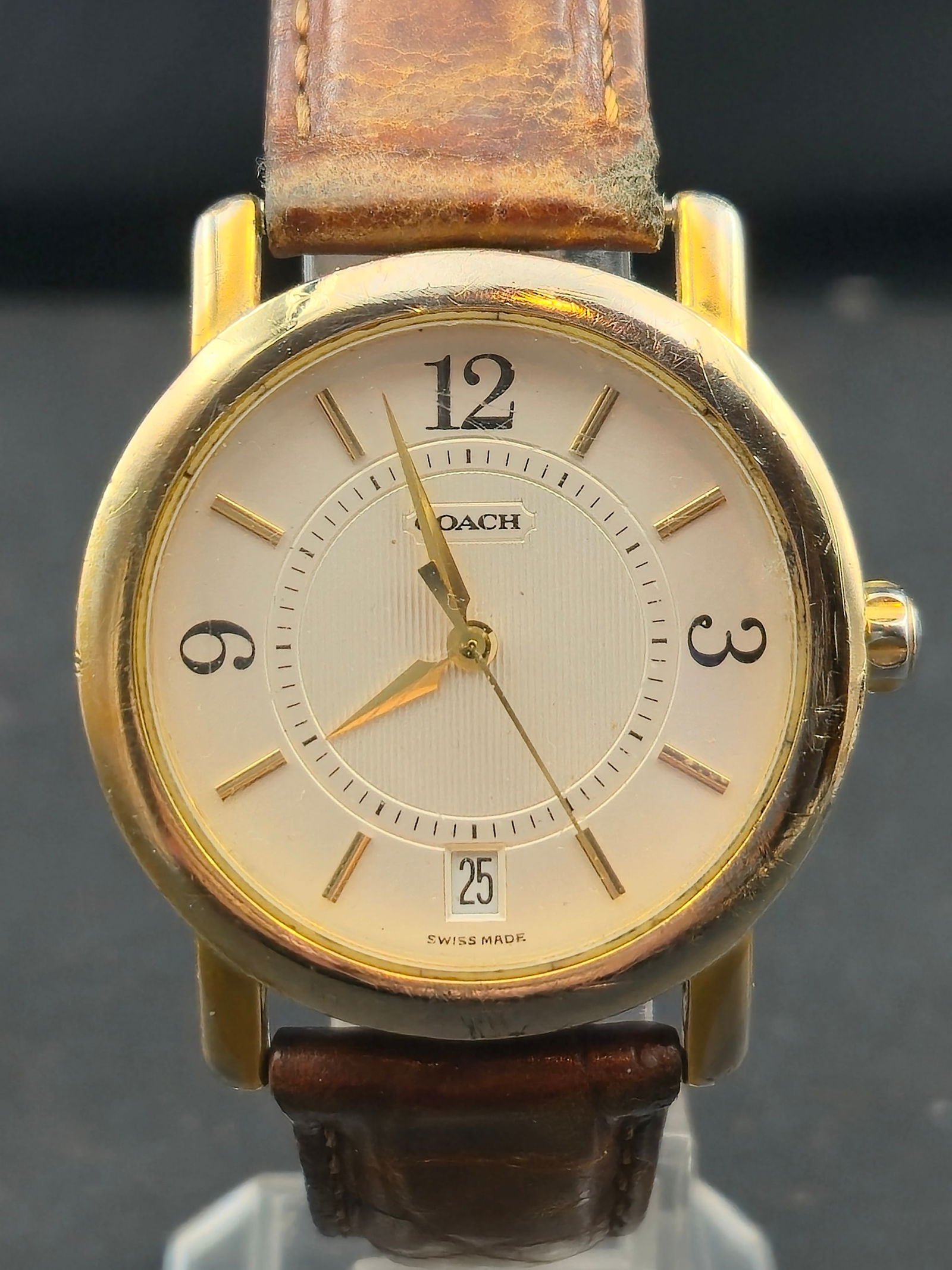 Coach W505 Swiss Made Gold-Tone Quartz Dress Watch: Elegant vintage Coach Swiss-made wristwatch featuring a classic gold-tone round case and minimalist white dial with bold Arabic numerals at 12, 3, and 9. Date window positioned at 6 o’clock. The wat