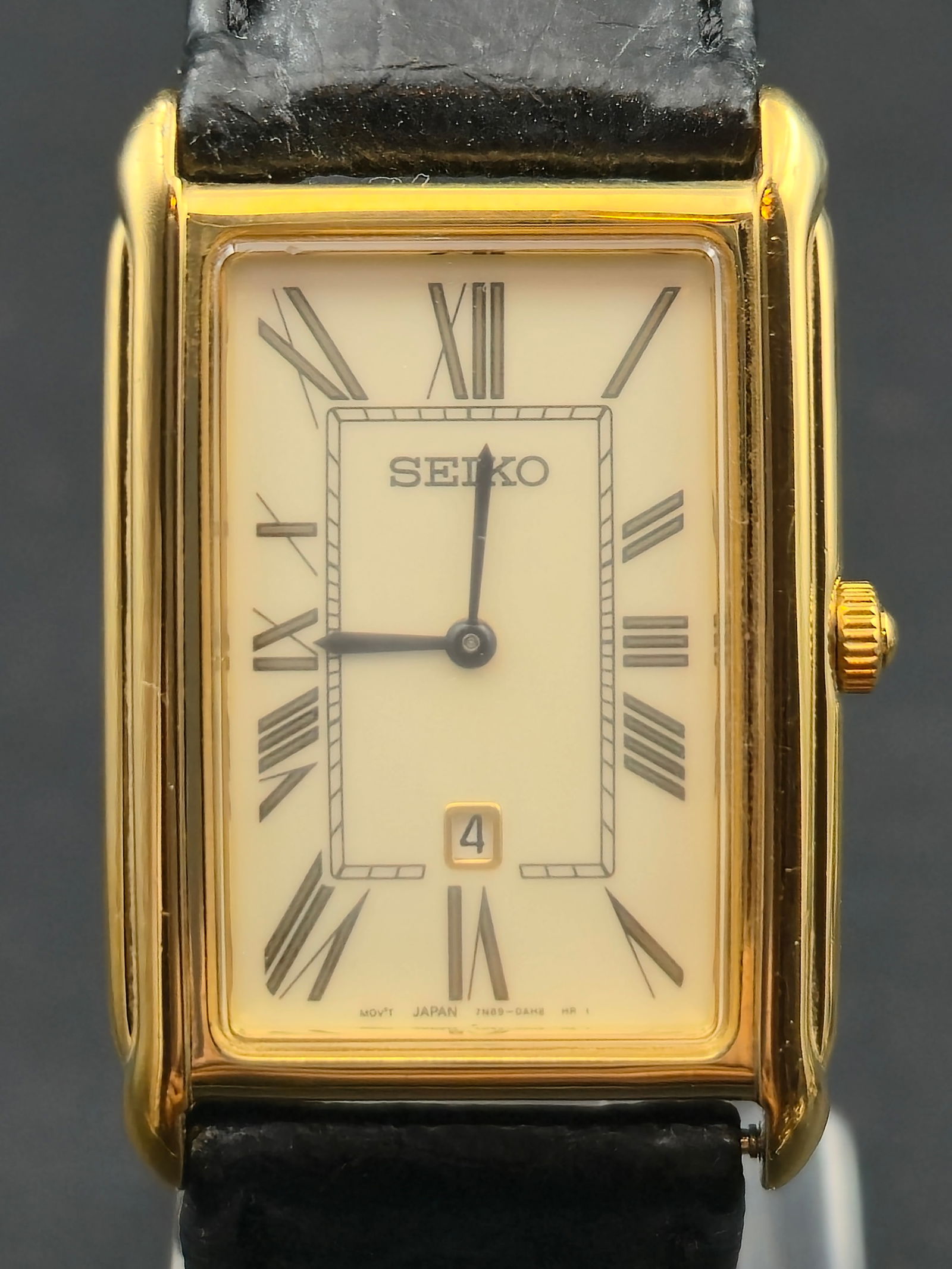 Seiko 7N89-0AD0 Gold-Tone Rectangular Quartz “Tank-Style” Watch: Elegant vintage Seiko quartz wristwatch in a refined gold-tone rectangular “Tank-style” case. The cream dial features Roman numeral hour markers and a framed inner minute track, complemented b