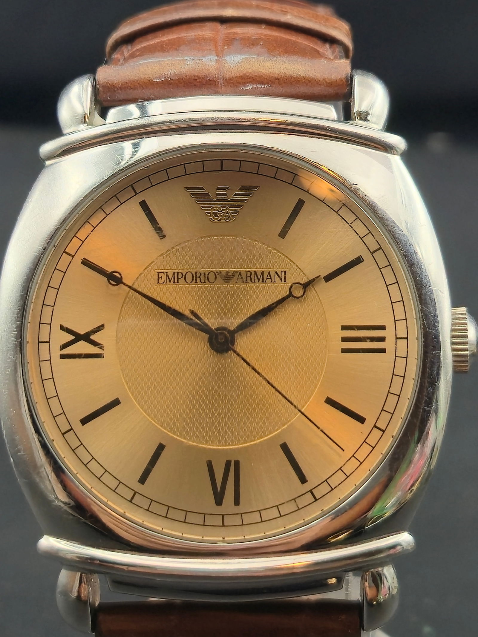 Emporio Armani AR-0264 Stainless Steel Gold Dial Men’s Watch – Runs (40mm): refined Emporio Armani men’s wristwatch featuring a cushion-shaped polished stainless-steel case paired with a warm champagne-gold dial and elegant Roman numeral hour markers. Its timeless design is