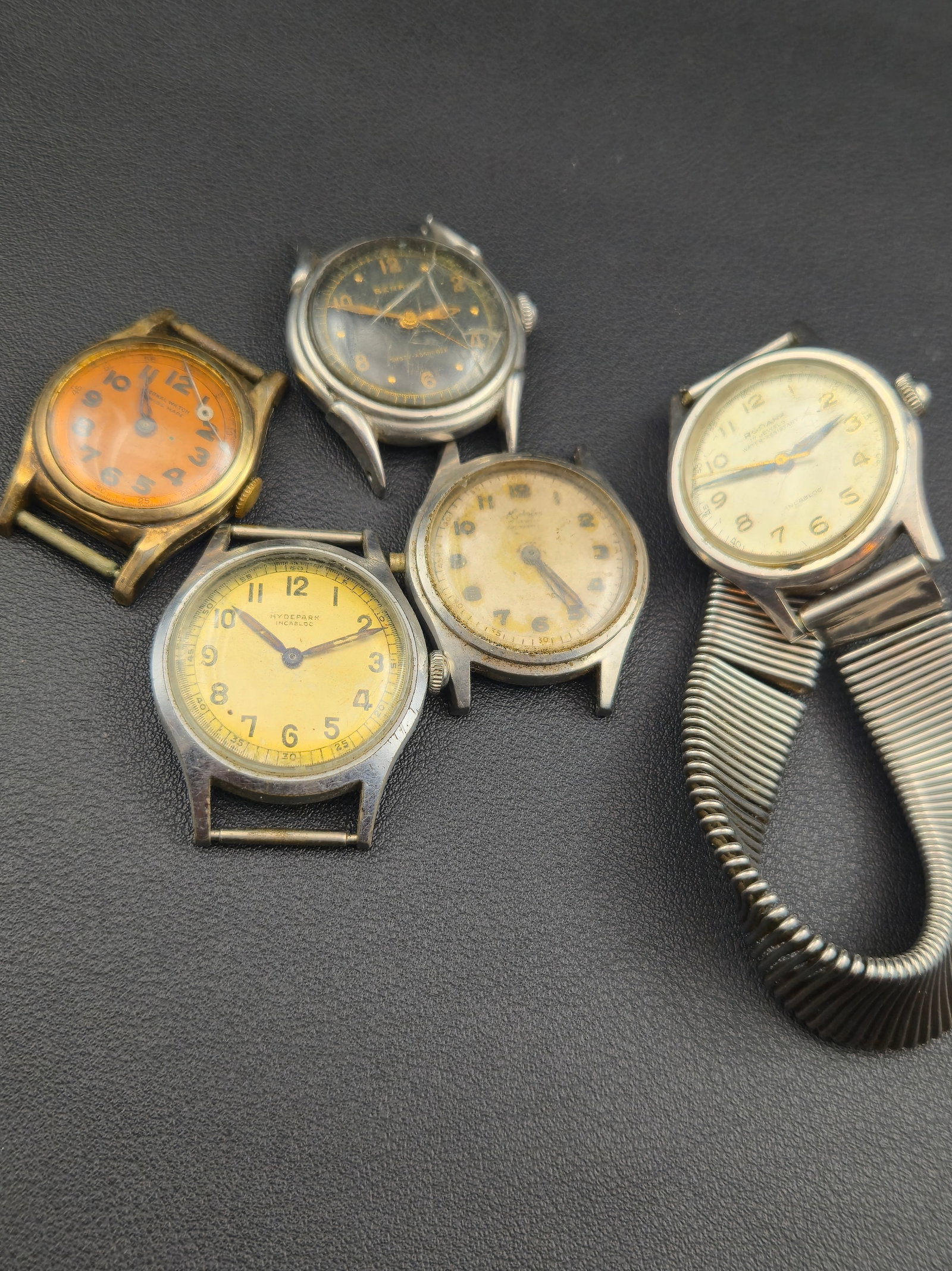 A lot of five vintage Swiss mechanical wristwatches featuring mid-century military-style and dress d: Rodana 17 Jewels Incabloc (c.1950s)Brand: RodanaEra: 1950sCase Size: 33 mmCase Material: Stainless steelMovement: Swiss 17-jewel manual wind (untested)Dial: Cream with luminous numerals and blue hands