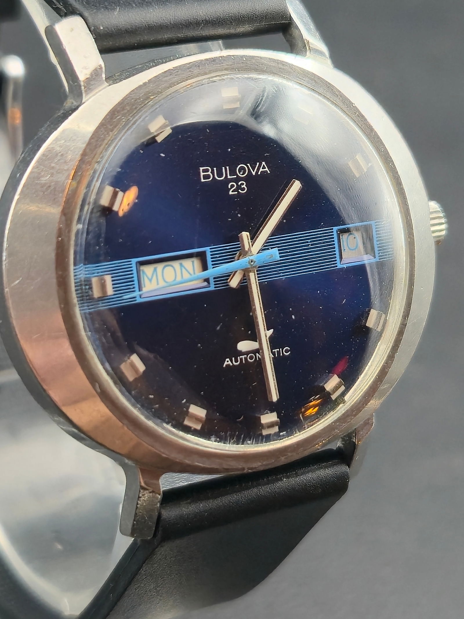 1972 Bulova 23 Automatic Blue TV Dial Stainless Steel 38 mm Wristwatch: Vintage Bulova 23 automatic wristwatch from 1972 featuring a metallic blue TV style dial with horizontal striped day and date windows at 3 oclock and 9 oclock. The watch houses Bulovas 23 jewel automa
