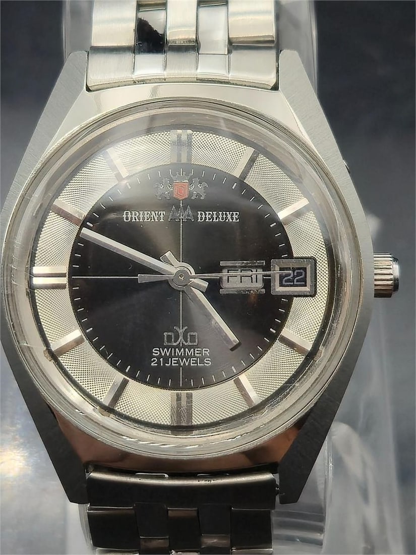 Orient AAA Deluxe DXO Swimmer 21J Auto Watch: This vintage Orient AAA Deluxe “Swimmer” wristwatch is a striking example of Japanese mechanical design from the post-1960s era. Featuring a black and silver textured dial with applied hour ma