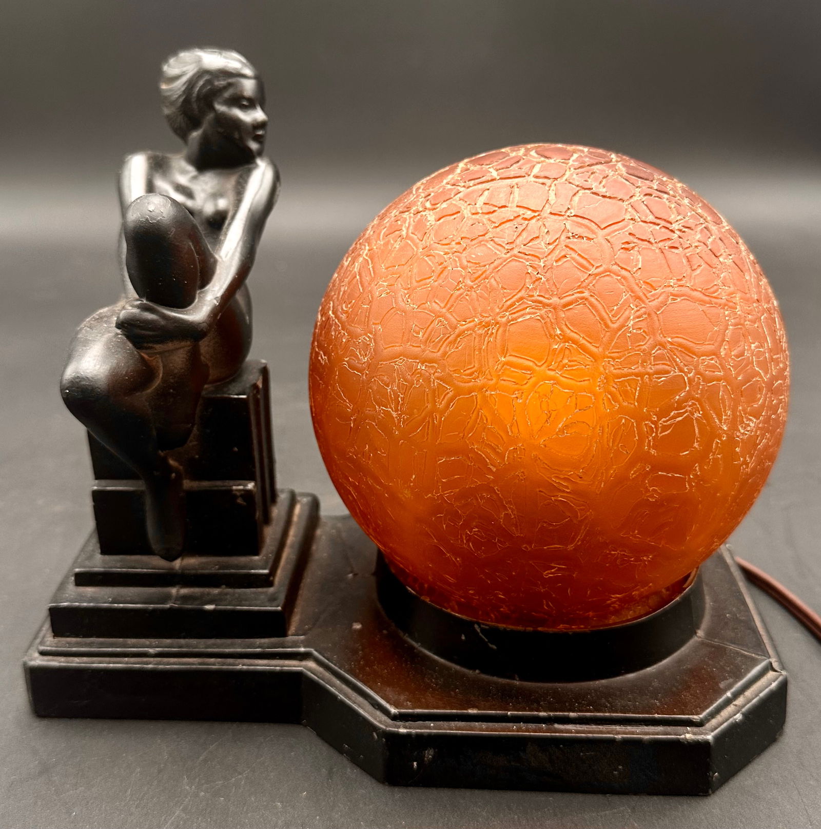 Art Deco Frankart Nuart Nude Lady Figural Lamp with Amber Crackle Glass Globe, c.1930s: Elegant vintage Art Deco lamp featuring a seated nude female figure in black-painted metal or spelter, mounted on a tiered geometric base. The lamp is paired with a striking amber crackle glass globe