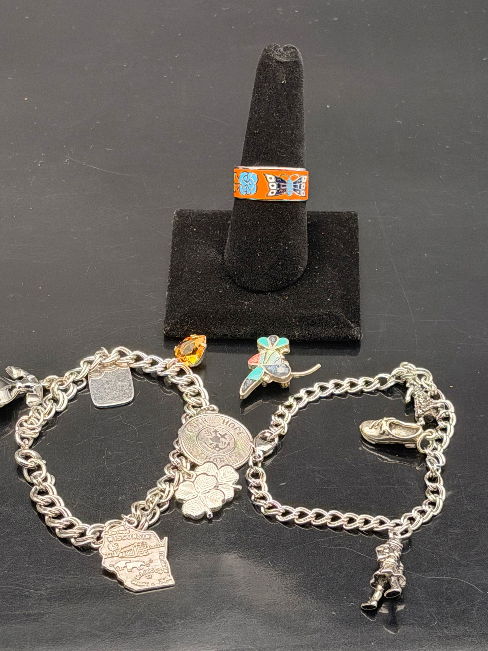 Vintage Silver Charm Bracelet Lot & Enamel Butterfly Ring – Wisconsin, Faith, Angel Charms (39g): Charming vintage mixed jewelry set featuring two silver-tone charm bracelets and one colorful enamel ring.Includes:•Two silver charm bracelets with unique themed charms — including Wisconsin st