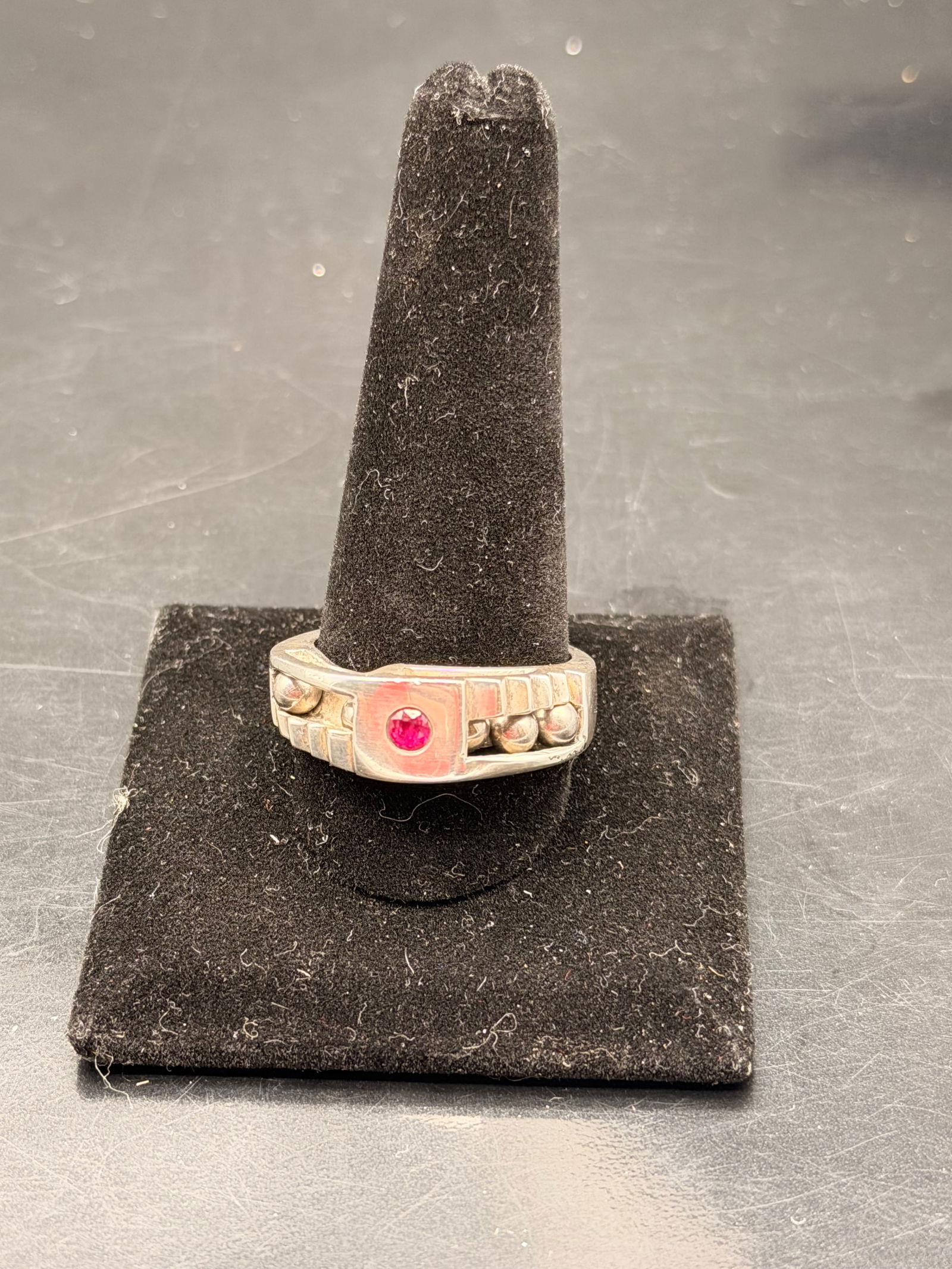 A wide-band silver ring with a red gemstone appears to be a men's signet or statement ring. (1 of 7)