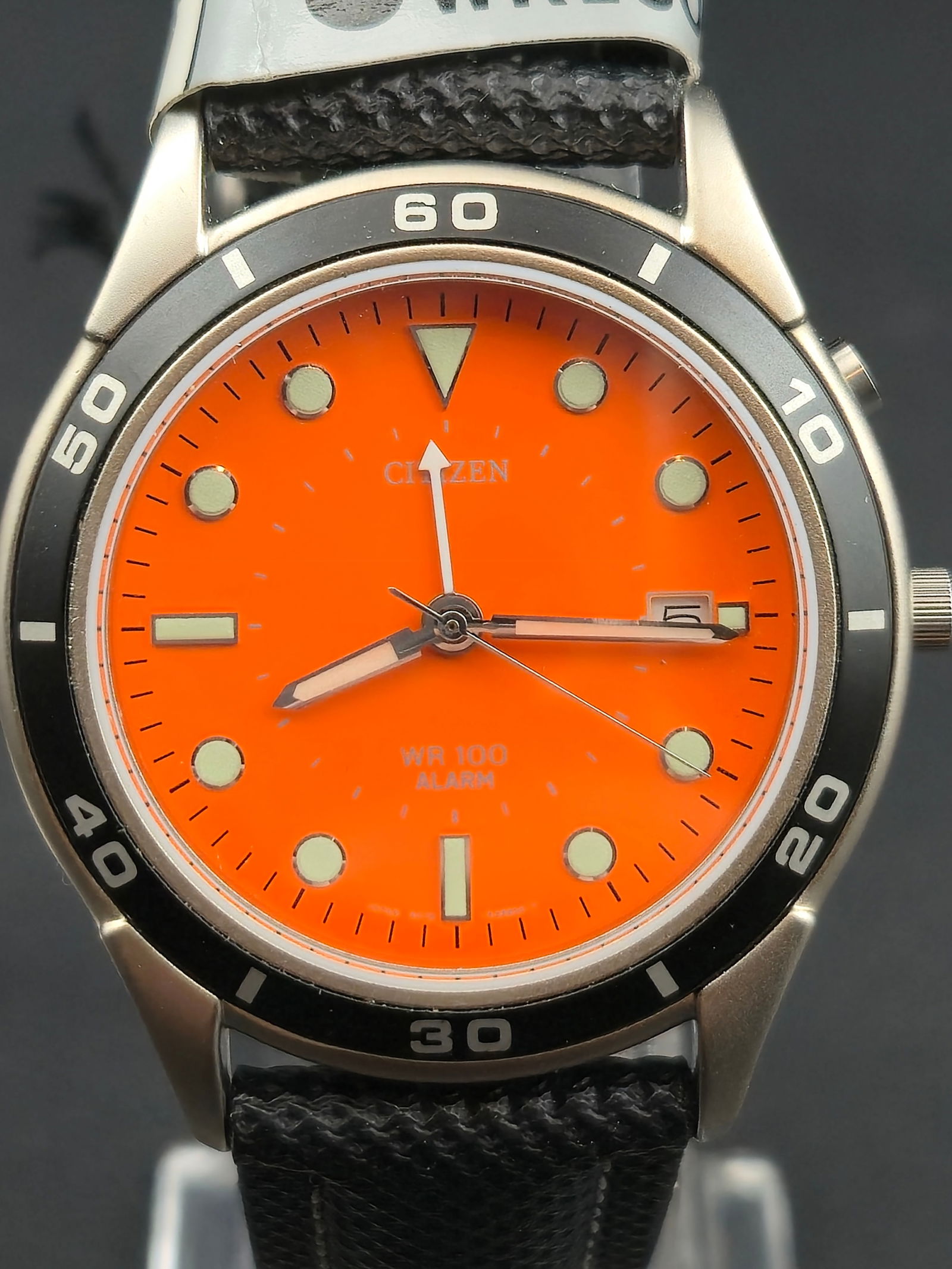 Citizen WR100 Alarm Orange Dial 39mm Quartz Watch – NOS, New Battery: This new old stock Citizen WR100 Alarm quartz watch features a striking bright orange dial with luminous hands and indices, black diver-style bezel, and stainless steel case measuring 39 mm. The watch