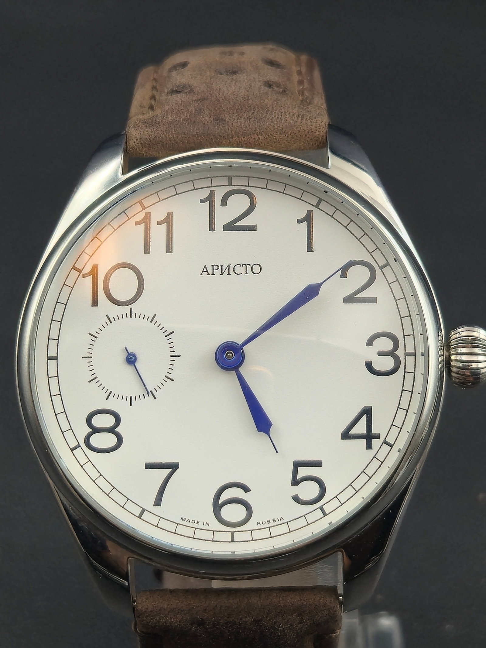 Aristo 18-Jewel Hand-Wind Mechanical 45 mm Display Back Pilot Watch – NOS: This Aristo wristwatch features a clean pilot-style white dial with Arabic numerals, blued steel hands, and a small-seconds subdial at 9 o’clock. The clear exhibition caseback reveals a Swiss-made 1