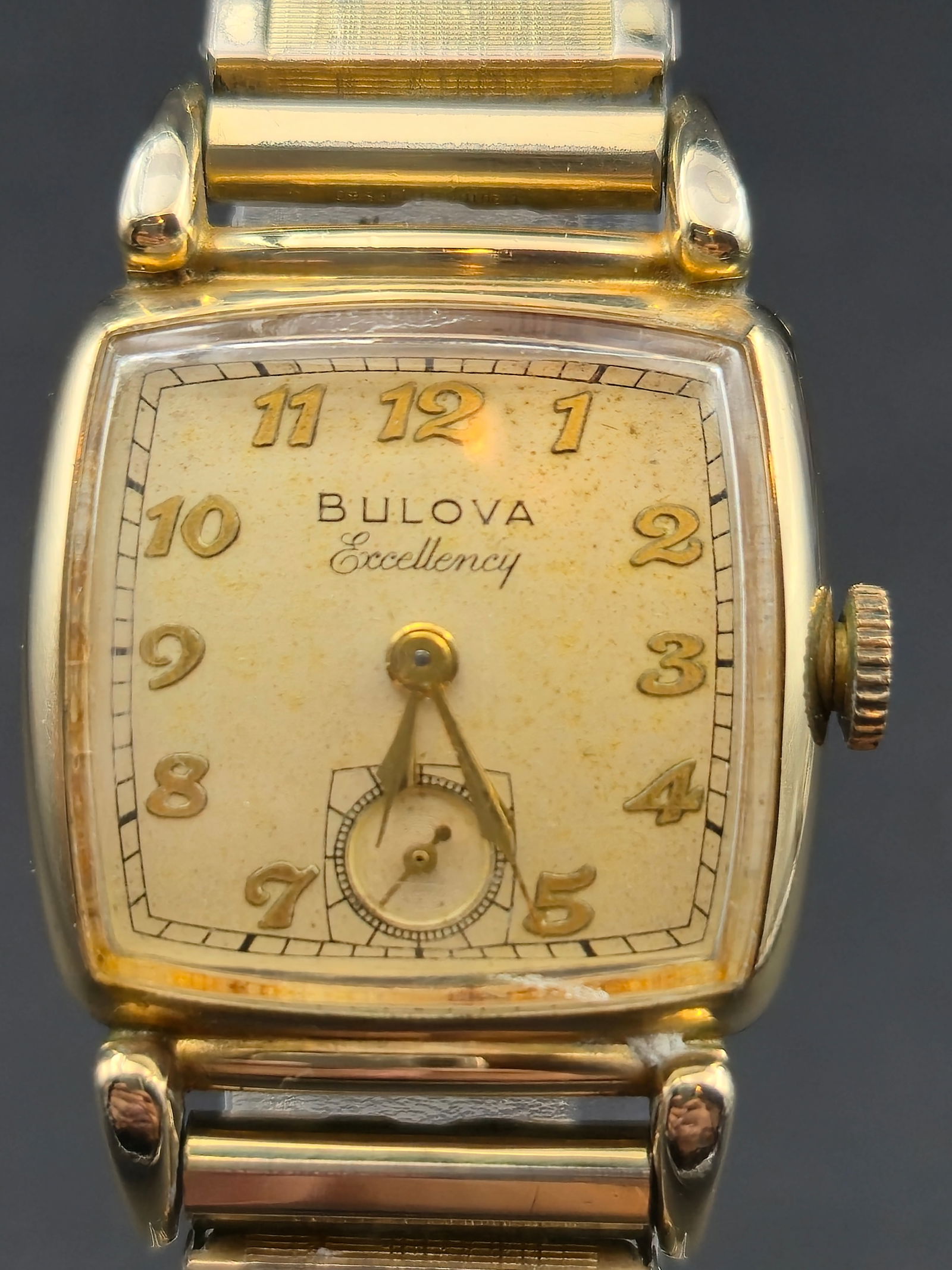 Bulova Excellency 10K Gold-Filled 26 mm 21J Manual Wind Dress Watch (1951) – Runs: Elegant vintage Bulova Excellency men’s wristwatch, dated L1 (1951), featuring a square-curved 10K gold-filled case with classic 1950s styling. The warm champagne dial retains its applied gold Arabi