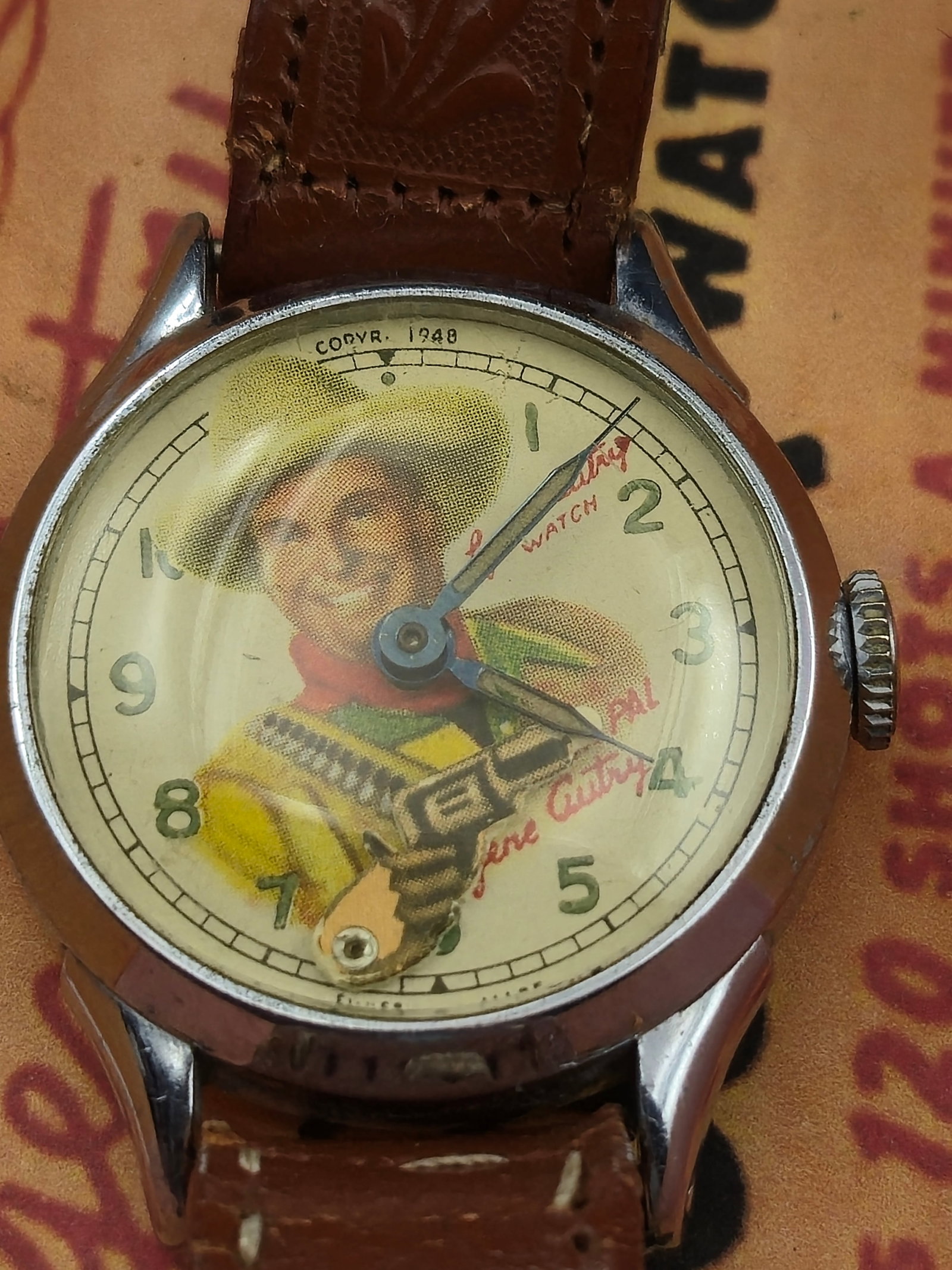 1948 Gene Autry Six Shooter Watch with Original Box Swiss Made Cowboy Dial Runs: Original 1948 Gene Autry “Six Shooter” wristwatch with its rare original box and insert, featuring colorful Western graphics and the cowboy legend’s portrait. The dial depicts Gene Autry in 