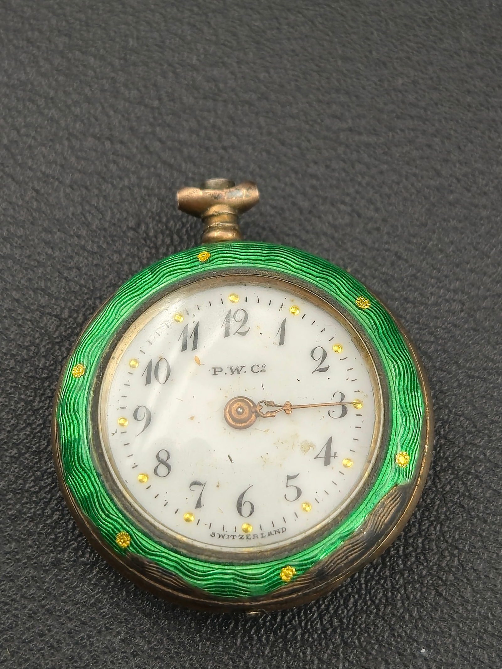 Swiss .800 Silver 26.9mm Green Guilloché Enamel Pendant Watch – P.W. Co.: Offered is a lovely Swiss .800 silver pendant watch by P.W. Co. / Paskar W. Co., featuring a vivid green guilloché enamel case with a hand-painted romantic scene on the reverse. The enamel is framed