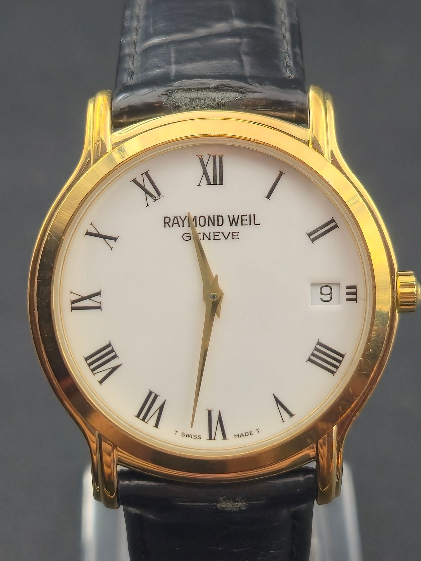 1990s Raymond Weil Genève 5569 “Classic Roman” 34mm Gold-Tone Swiss Quartz Watch – New: A refined 1990s Raymond Weil Genève reference 5569 featuring the elegant “Classic Roman” design with a white dial, black Roman numeral markers, and gold-tone hands. Powered by a 7-jewel Swiss