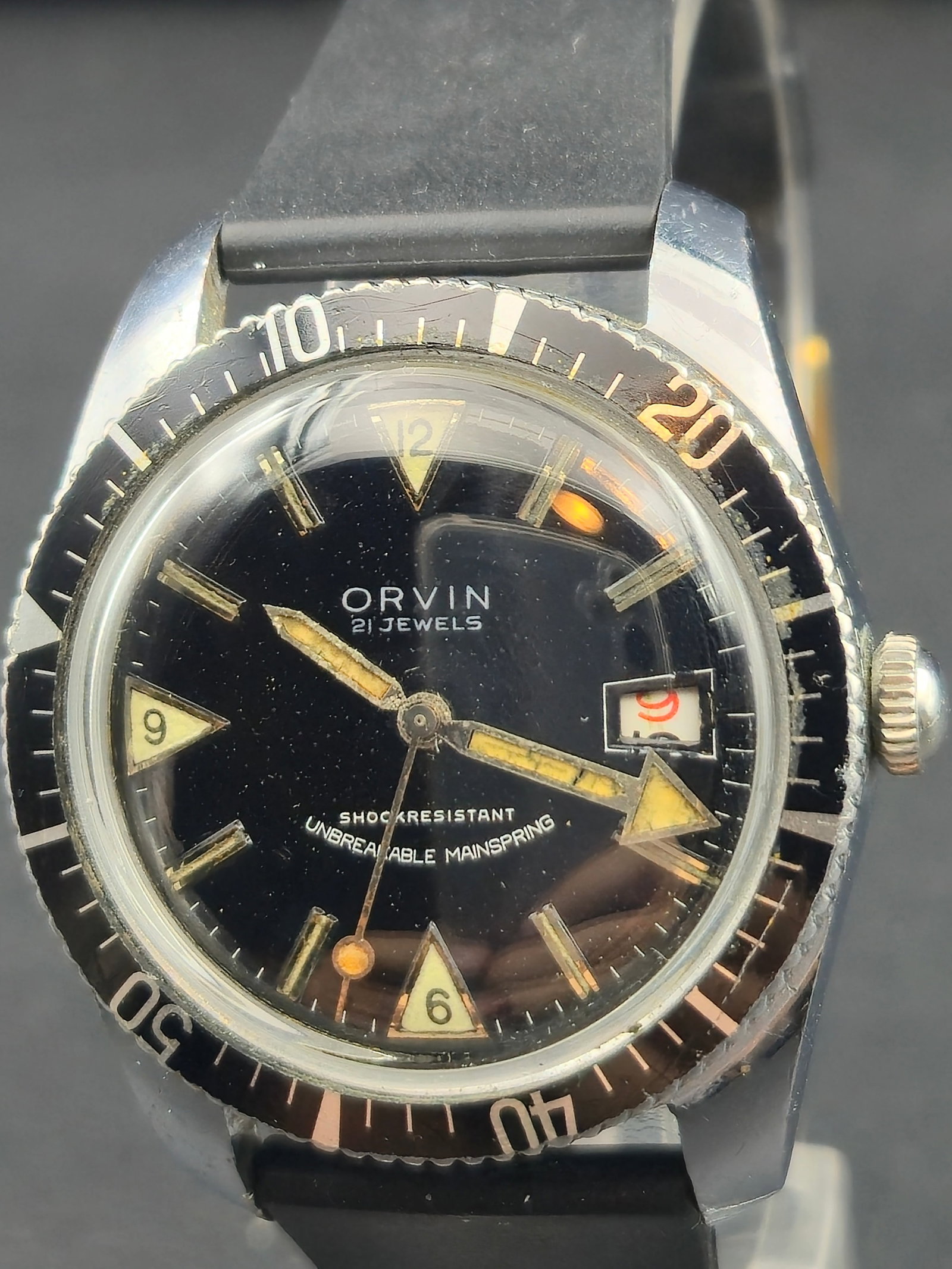 1960s Orvin 35mm Diver-Style 21J Mechanical Watch Black Dial: Vintage 1960s Orvin 21-jewel mechanical diver-style wristwatch featuring a classic black dial with lume-filled triangular markers, rotating bezel, and date window at 3. Powered by a 21-jewel hand-wind