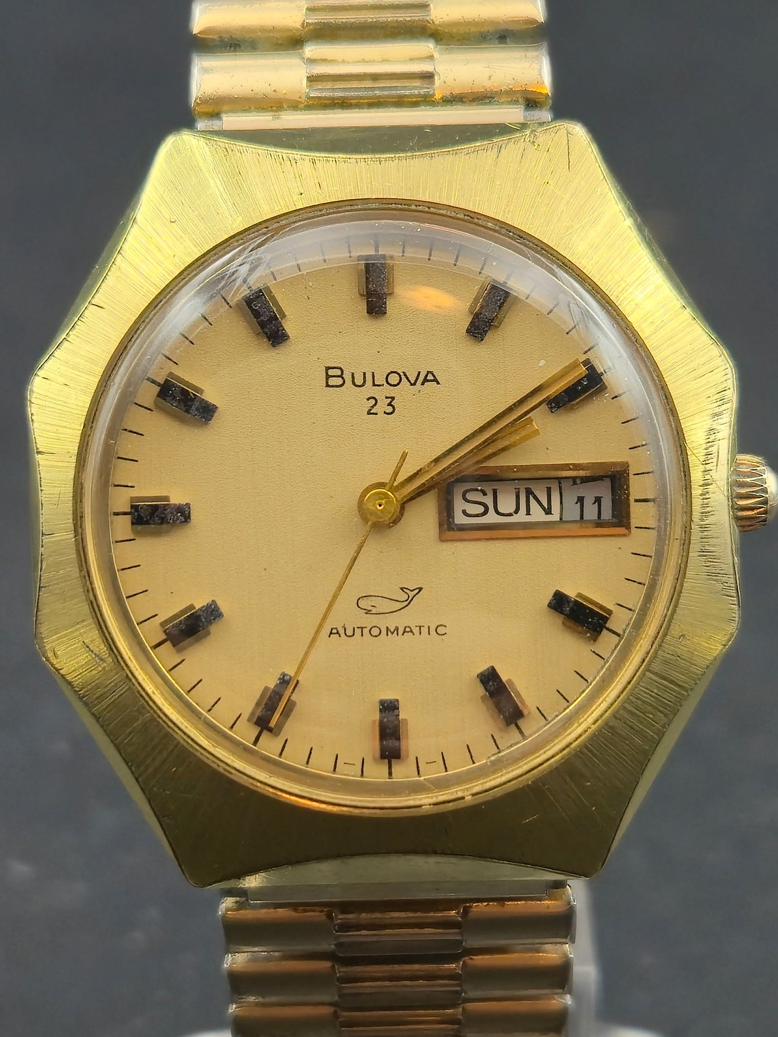 1962 Bulova 23 Automatic 36mm Gold Electroplate Bezel 10K RGP Back 23J Whale Logo Day Date Runs Vint: Vintage 1962 Bulova 23 Automatic featuring the desirable whale logo on the dial, a brushed gold-tone face with applied black/gold markers, and matching gold hands. The case uses a gold-electroplate be