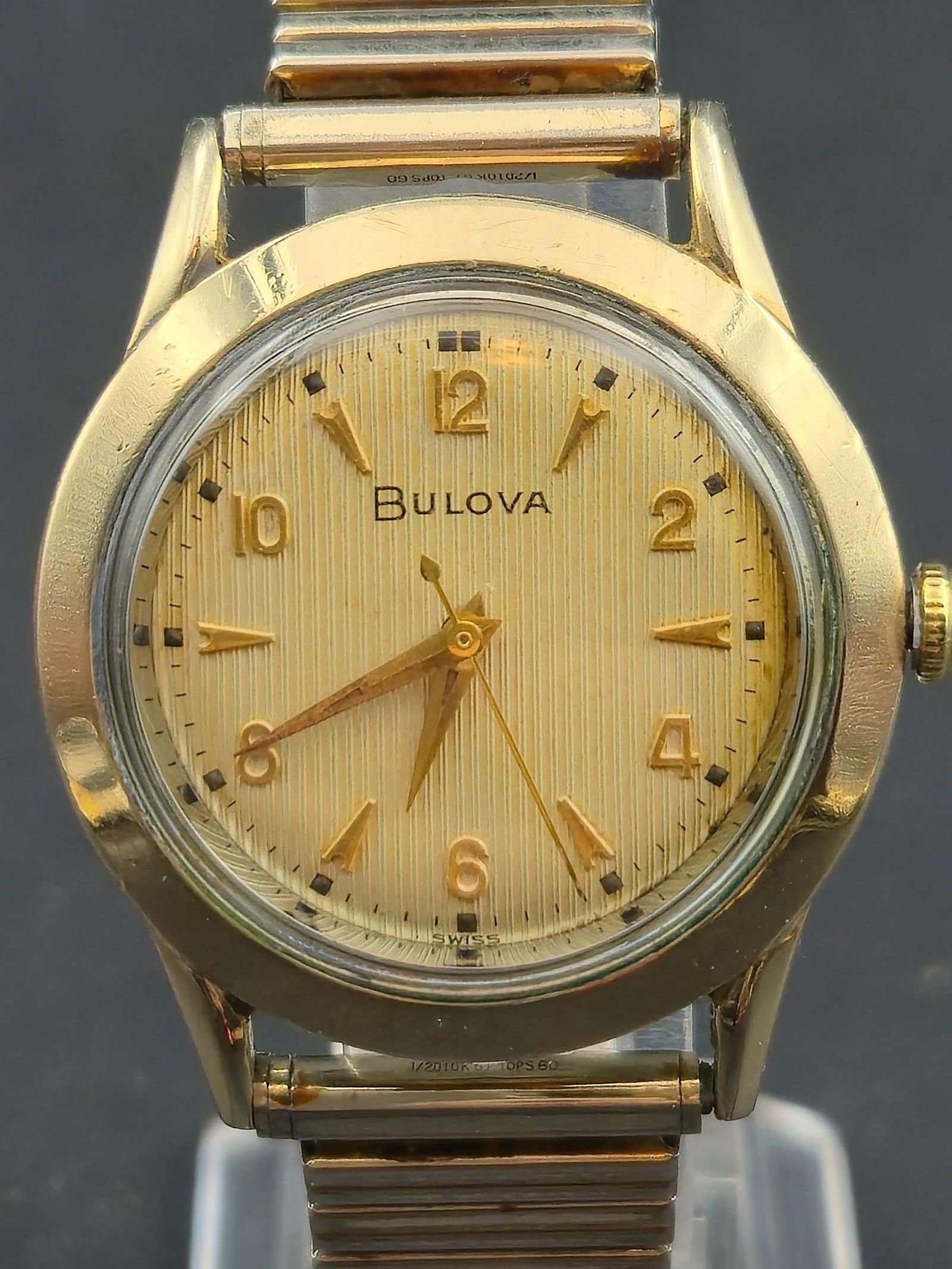 1954 Bulova 34mm 10K GF Ribbed Dial w/ 10BUC Movement & GF Top Caps Band – Runs: Vintage 1954 Bulova wristwatch featuring a vertically ribbed champagne dial with applied gold Arabic numerals and dagger markers. Caseback marked L4 confirming 1954 production. Powered by the clean Bu