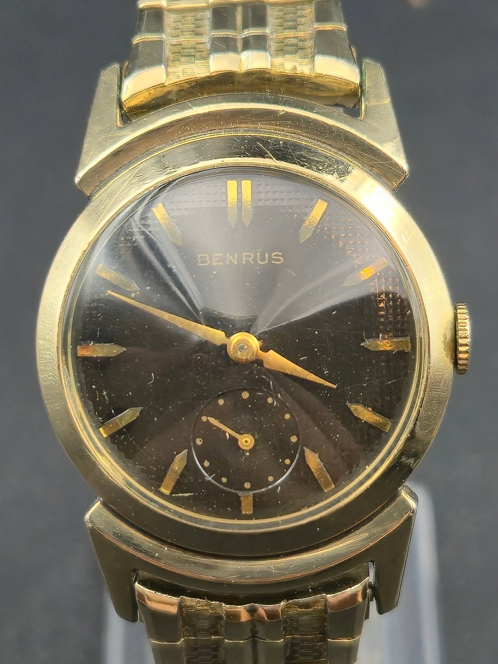 1950s Benrus 30mm 10K RGP “Mountain Peak” Lugs Textured black Dial GF Band – Running: Offered is a 1950s Benrus men’s wristwatch featuring the desirable “mountain peak” stepped lugs, a textured charcoal sunburst dial, and polished crystal. The watch is running, with smooth ba