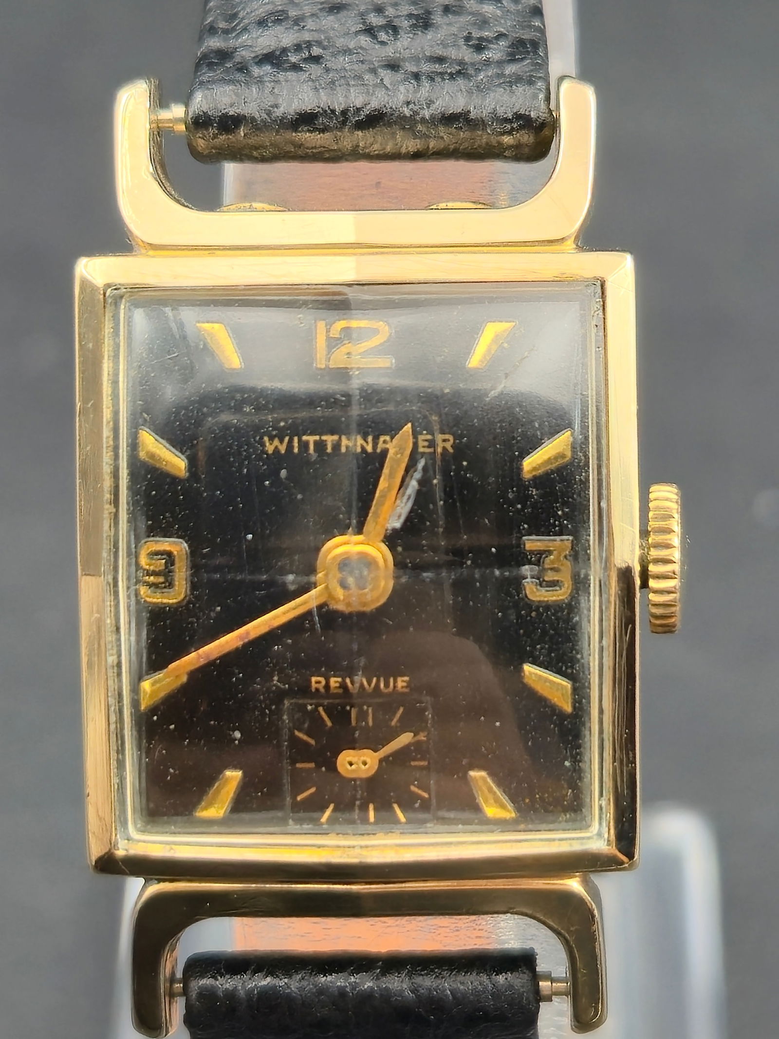 1950s Wittnauer Revue 10K GF Tank 21mm – Faceted Crystal – Running: This 1950s Wittnauer Revue features a beautifully preserved faceted period glass crystal over a striking black and gold Art Deco dial. The 10K gold filled tank case houses a Swiss Wittnauer 73 movemen